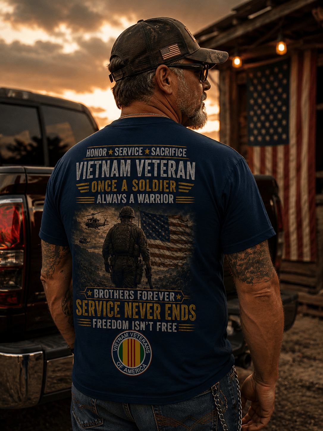 A man wearing a navy blue t-shirt with a large graphic print on the back. The graphic features a soldier, a helicopter, an American flag, and military-themed text including 'VIETNAM VETERAN' and 'SERVICE NEVER ENDS'.