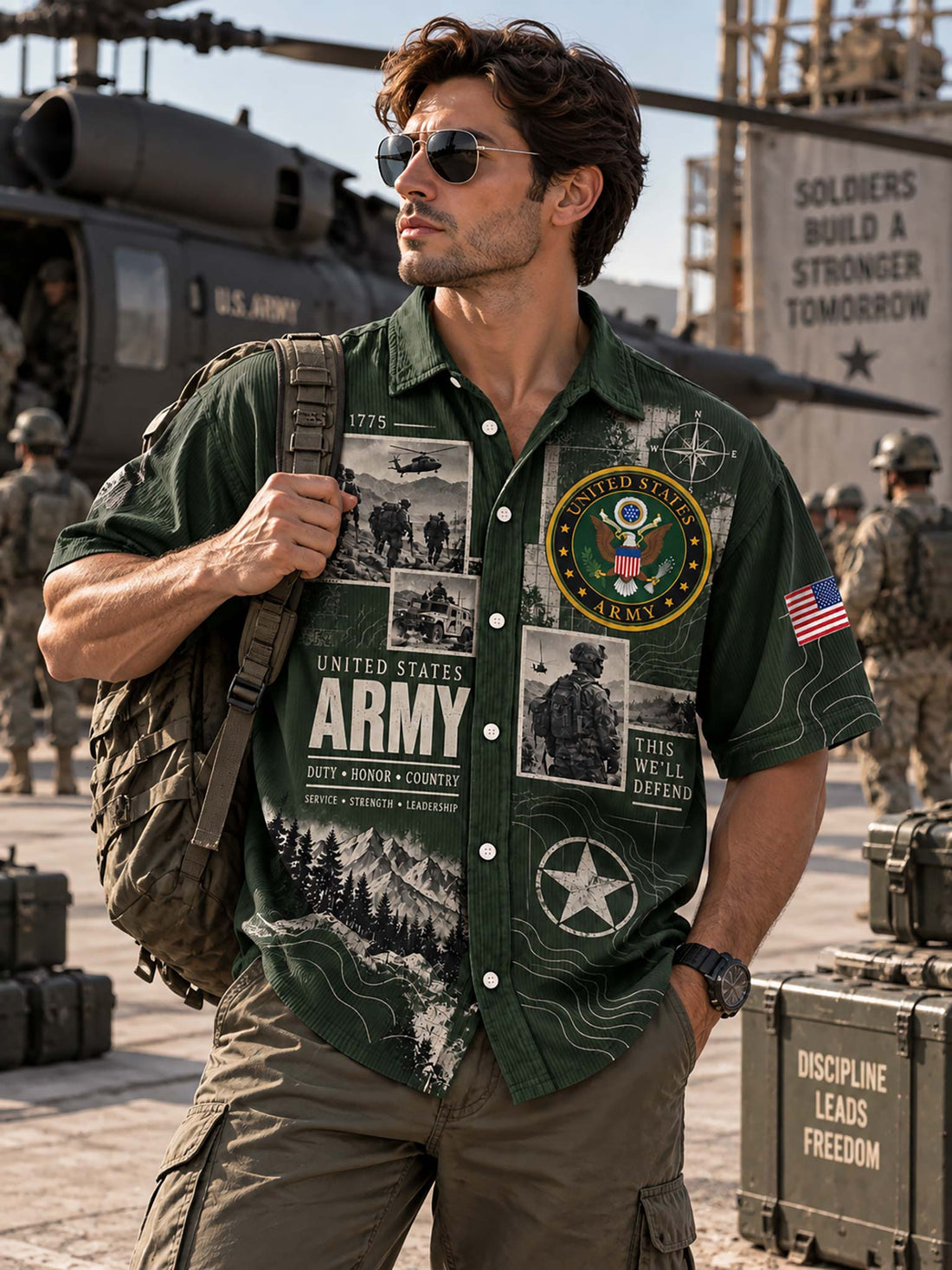 A man wearing a dark green short-sleeve button-up shirt with a detailed United States Army graphic print, paired with blue jeans, against a light gray background.