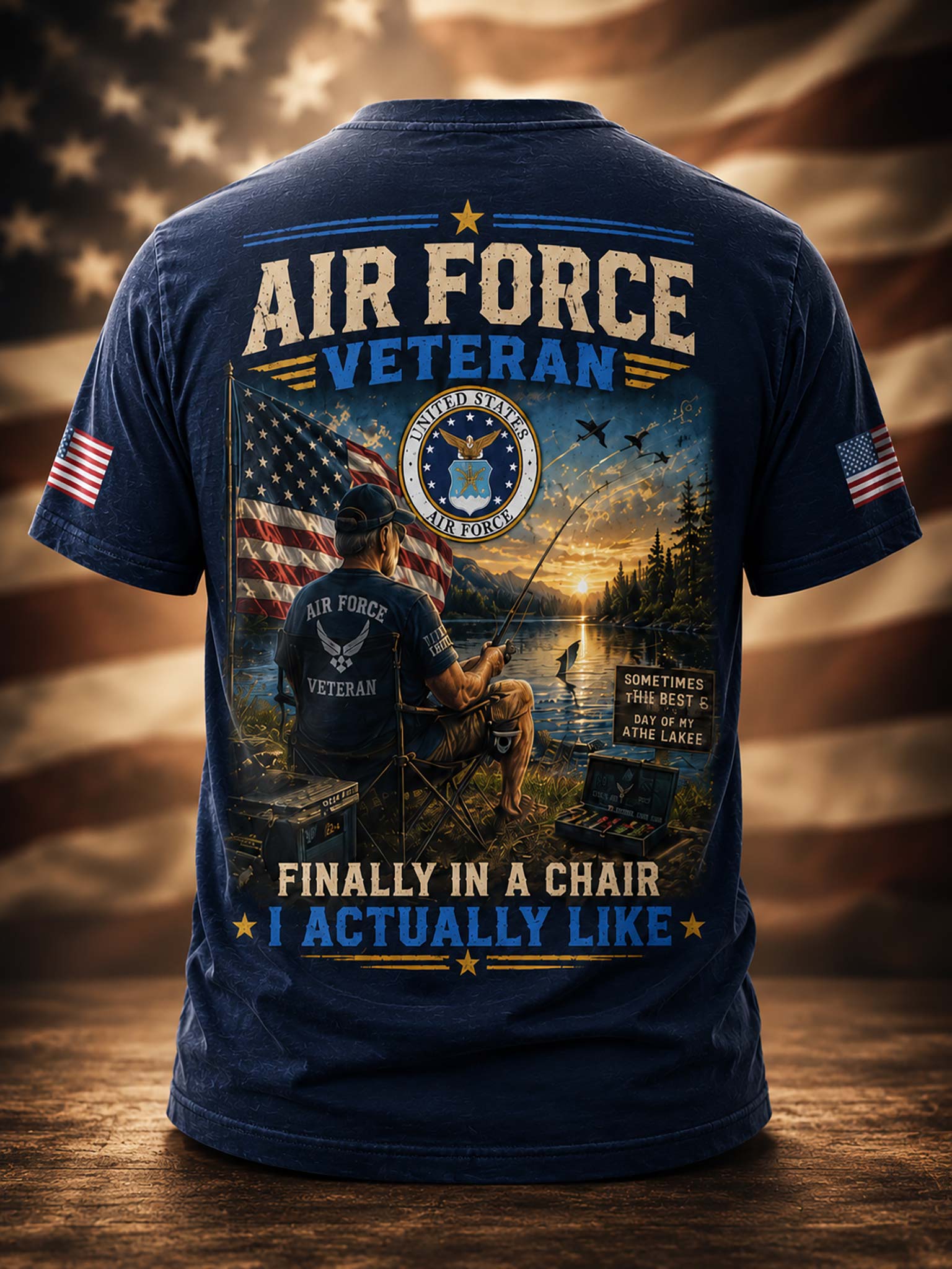 A navy blue short-sleeve t-shirt shown from the back, featuring a large patriotic graphic with the words 'AIR FORCE VETERAN' and 'FINALLY IN A CHAIR I ACTUALLY LIKE'. The print includes an American flag, a seated figure, a dog, a lake scene at sunset, and military insignia.