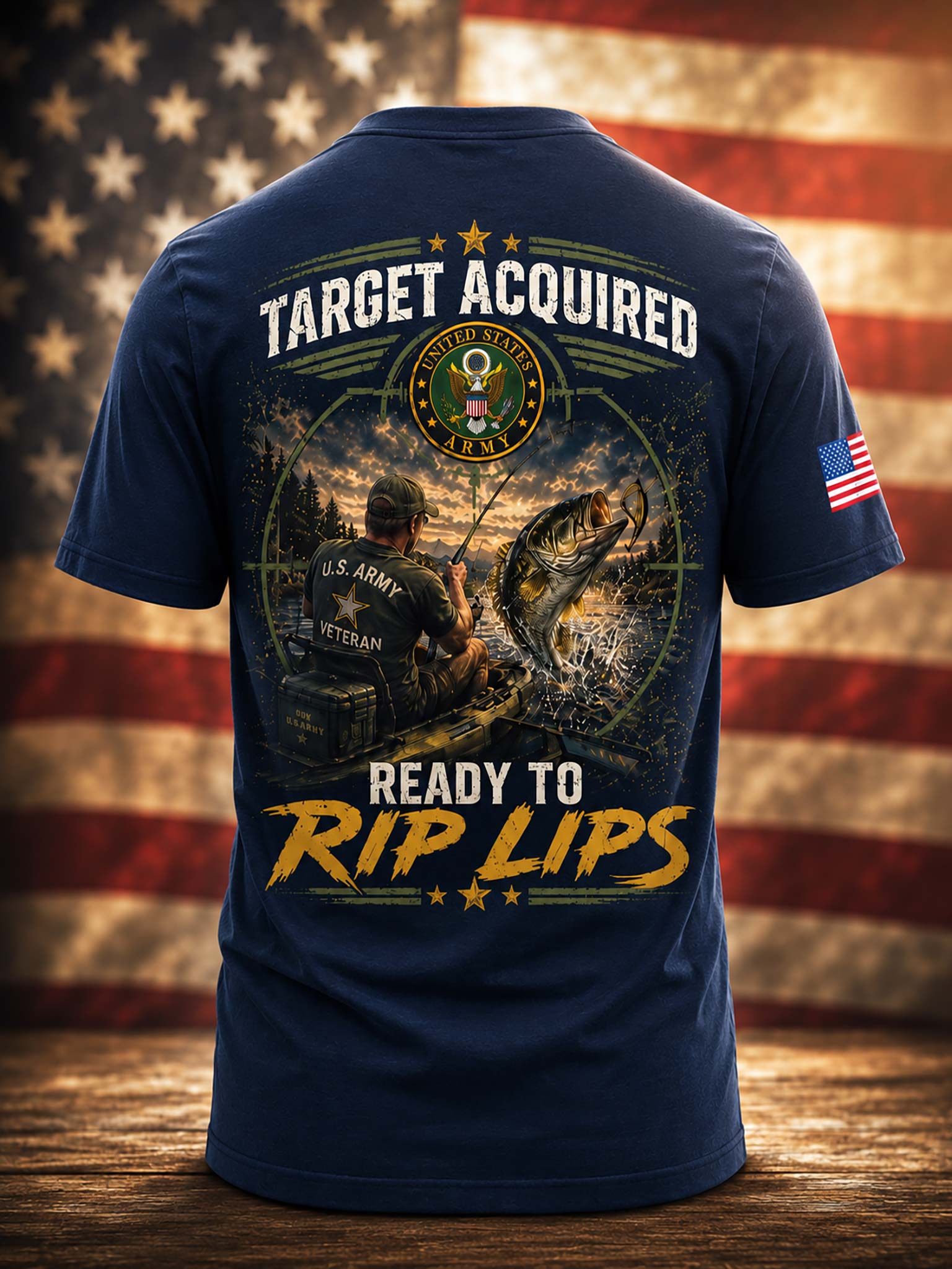 A navy blue short-sleeve t-shirt shown from the back, featuring a large graphic print with the text 'TARGET ACQUIRED' and 'READY TO RIP LIPS' around a fisherman and fish illustration. The shirt is displayed against a blurred American flag background on a wooden surface.