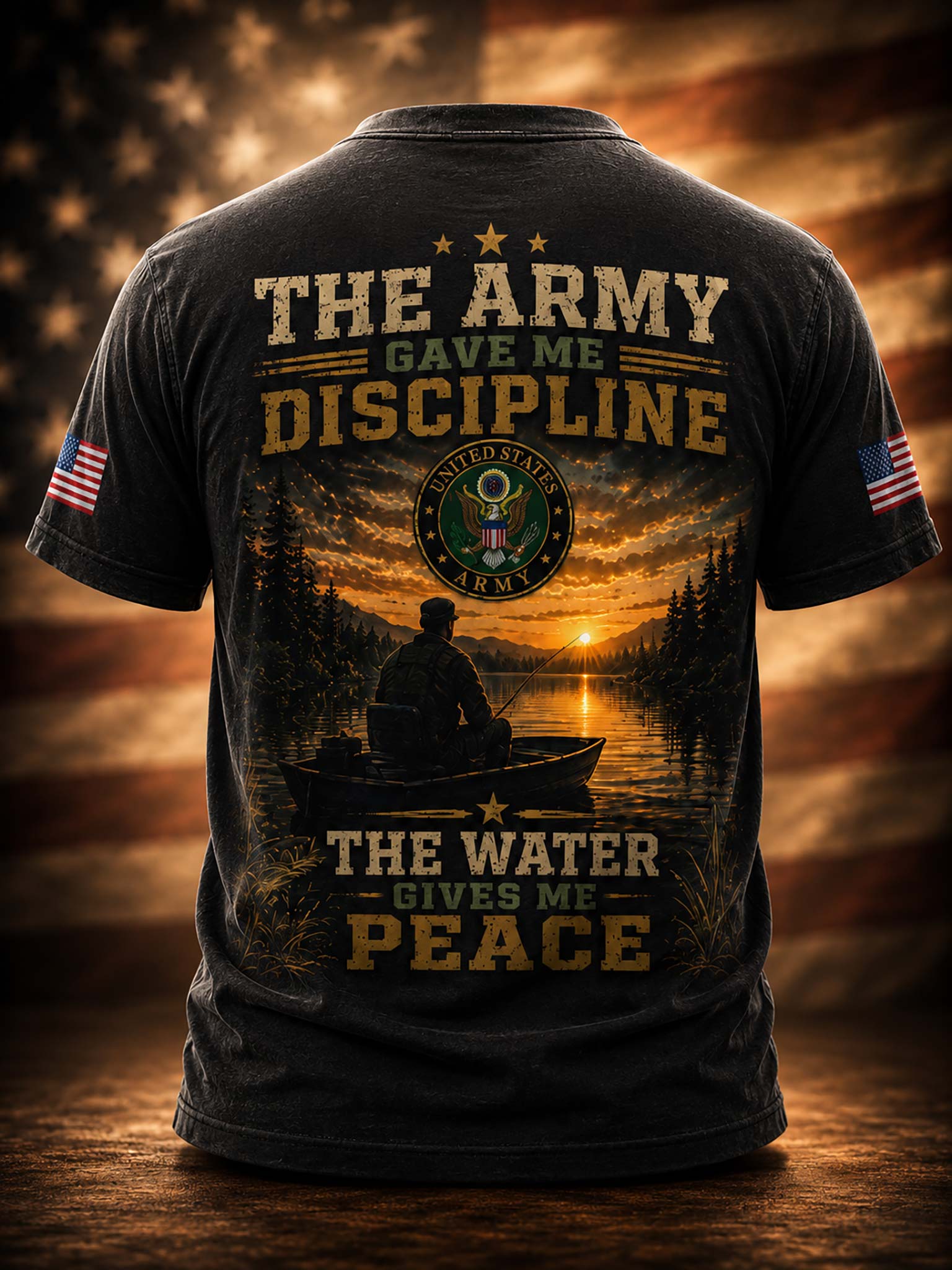A black graphic t-shirt shown from the back, featuring military-themed text, a sunset over water with a silhouetted figure in a boat, a circular emblem, and American flag patches on the sleeves. The shirt is centered against a dramatic, warm-toned blurred background.