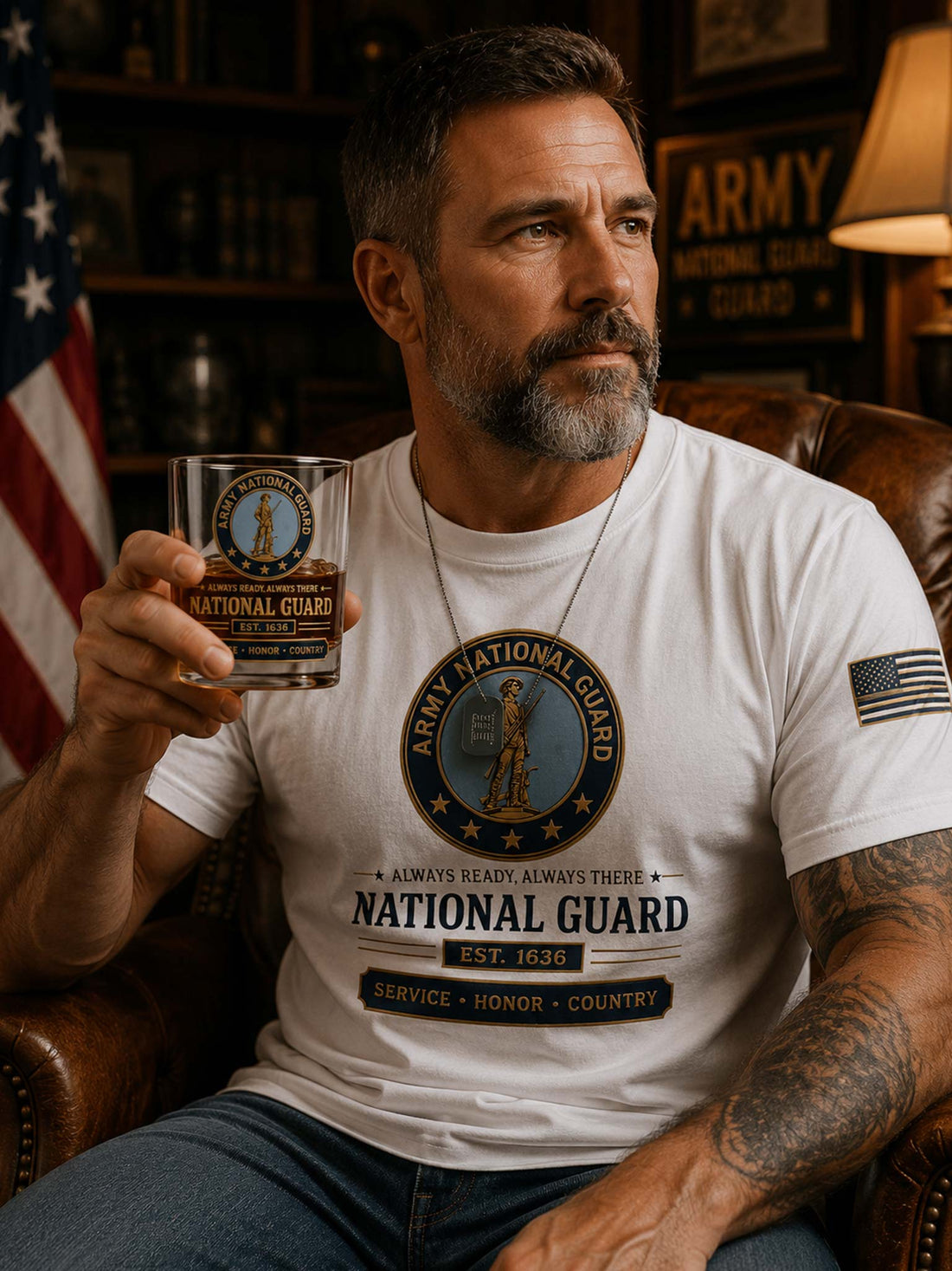 A clear whiskey tumbler glass with a printed Army National Guard emblem and text, filled with amber liquid, set on a dark wooden coaster against a black background.