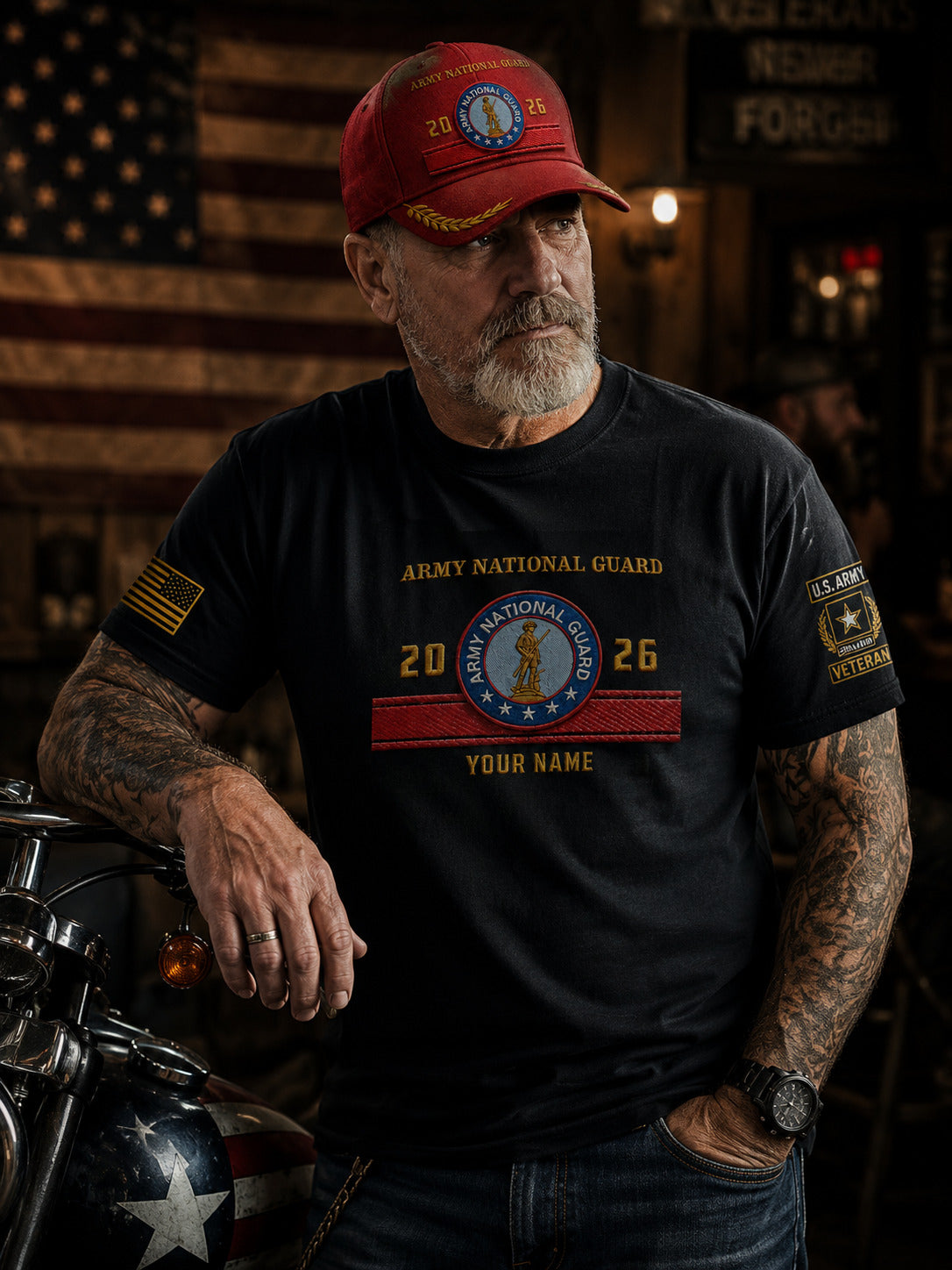 A man with a gray beard and tattoos wearing a black Army National Guard t-shirt and a red cap, leaning on a motorcycle in a rustic bar setting.