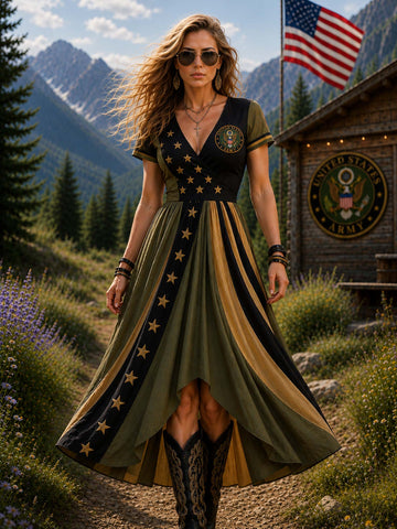 A woman wearing a military-inspired high-low dress with olive green and black panels, gold stars, and a gold central stripe, walking outdoors in front of mountains, a cabin, and an American flag.