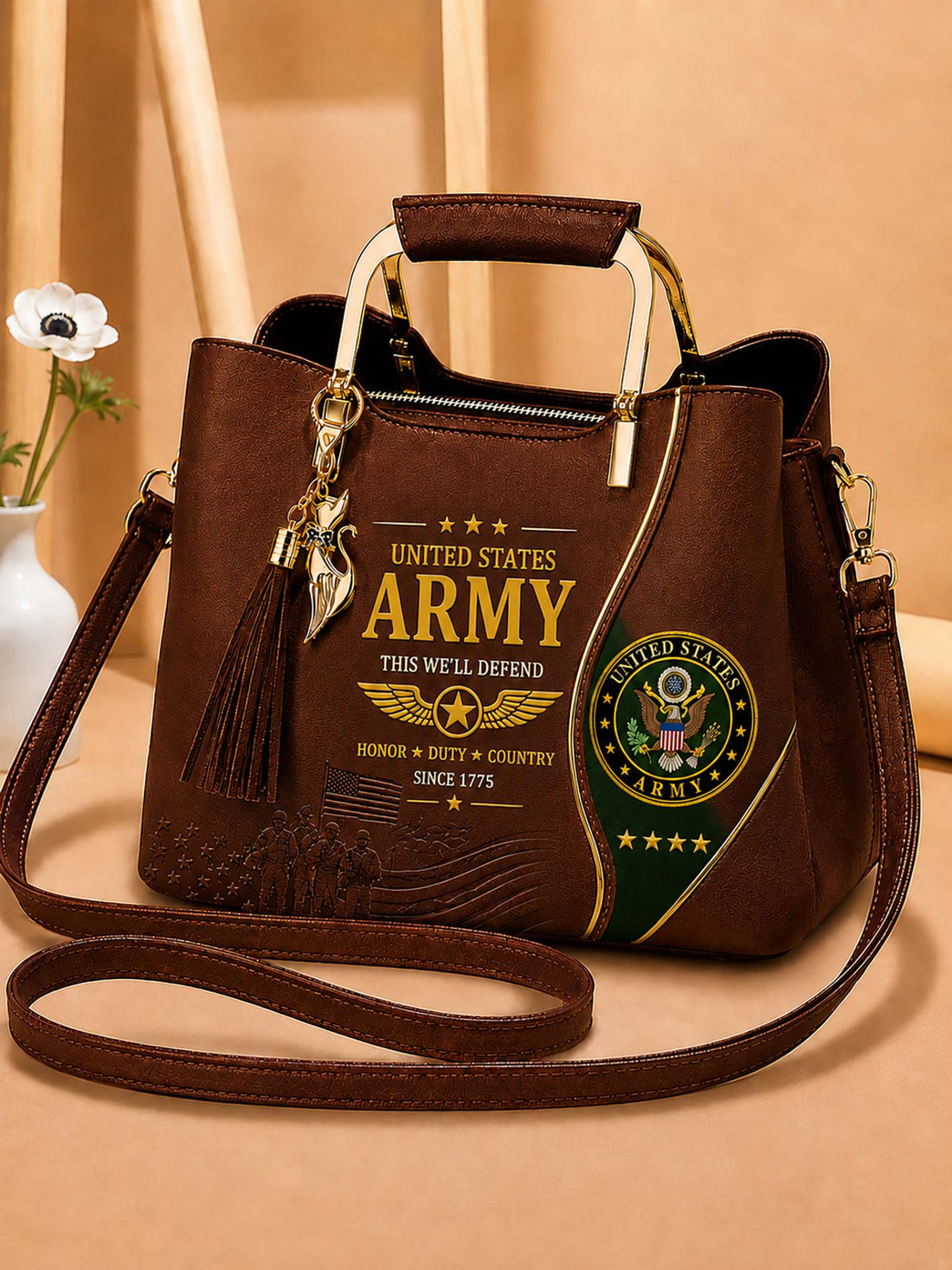 A brown faux-leather handbag with military-themed graphics, featuring 'United States Army' text, a gold eagle charm, a tassel, and a green and gold seal on the front. The bag has a top handle, a shoulder strap, and is set against a warm beige background.