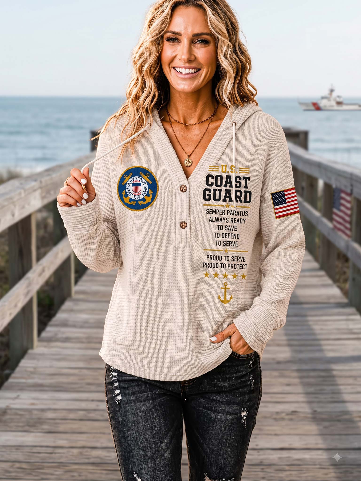A woman stands on a wooden dock by the ocean wearing a beige waffle-knit hoodie with U.S.