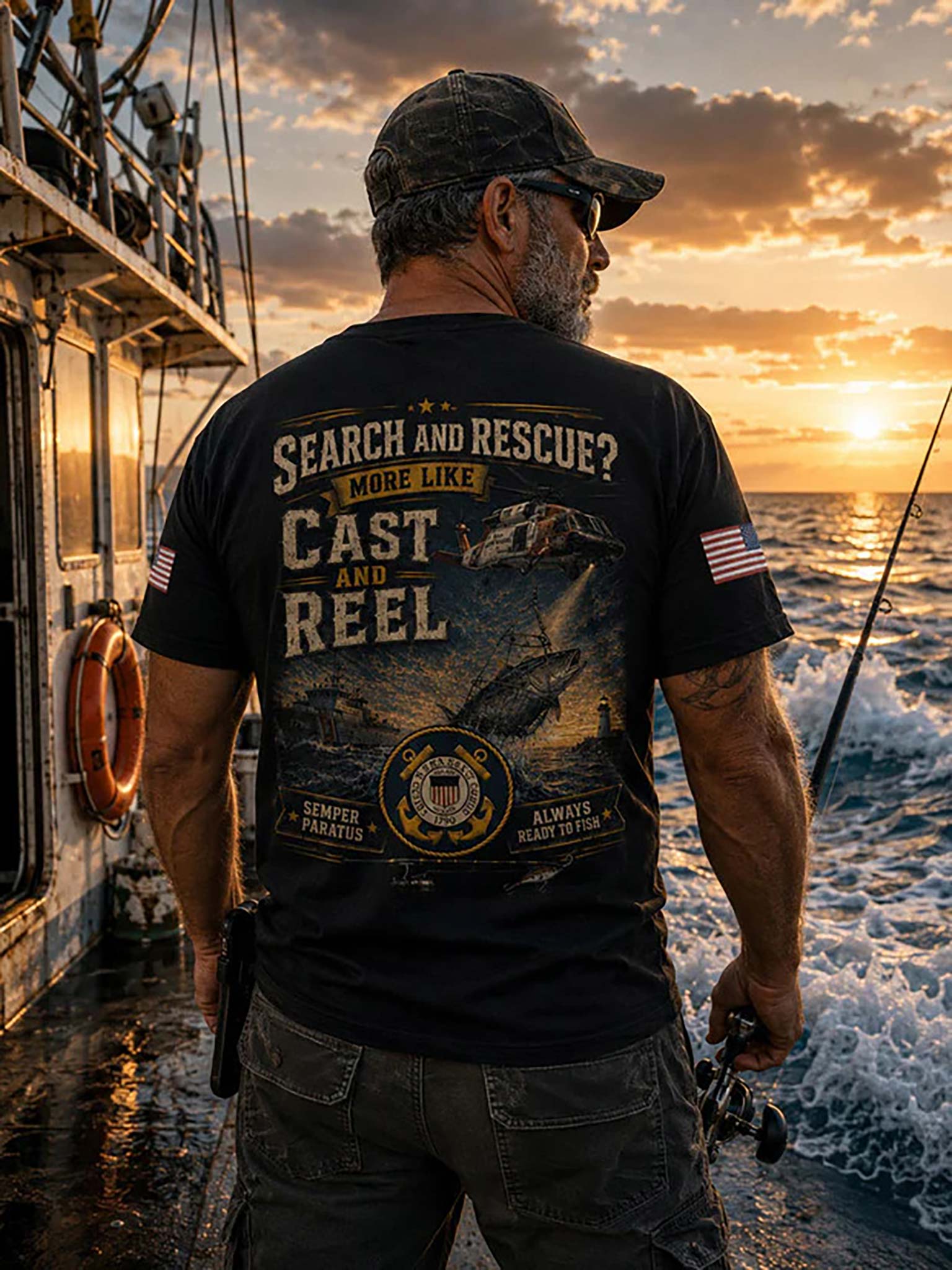 A man on a fishing boat at sunset, shown from behind wearing a black graphic t-shirt with 'SEARCH AND RESCUE? CAST AND REEL' printed on the back, along with a fish, a shark, and a US Coast Guard emblem.