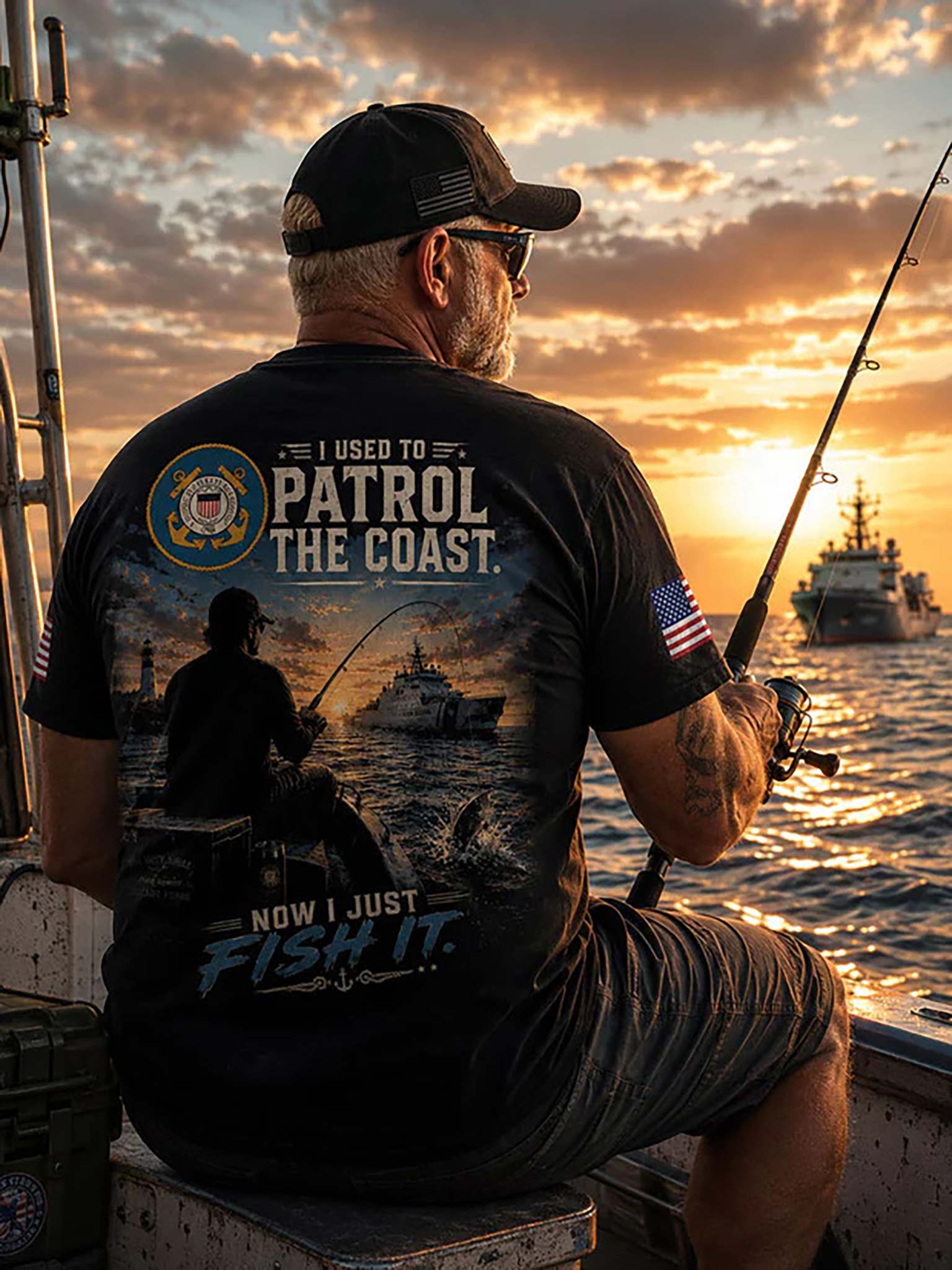 A man sitting on a boat at sunset, shown from behind wearing a black graphic t-shirt with a fishing and naval patrol design. The back of the shirt features the text 'I USED TO PATROL THE COAST.