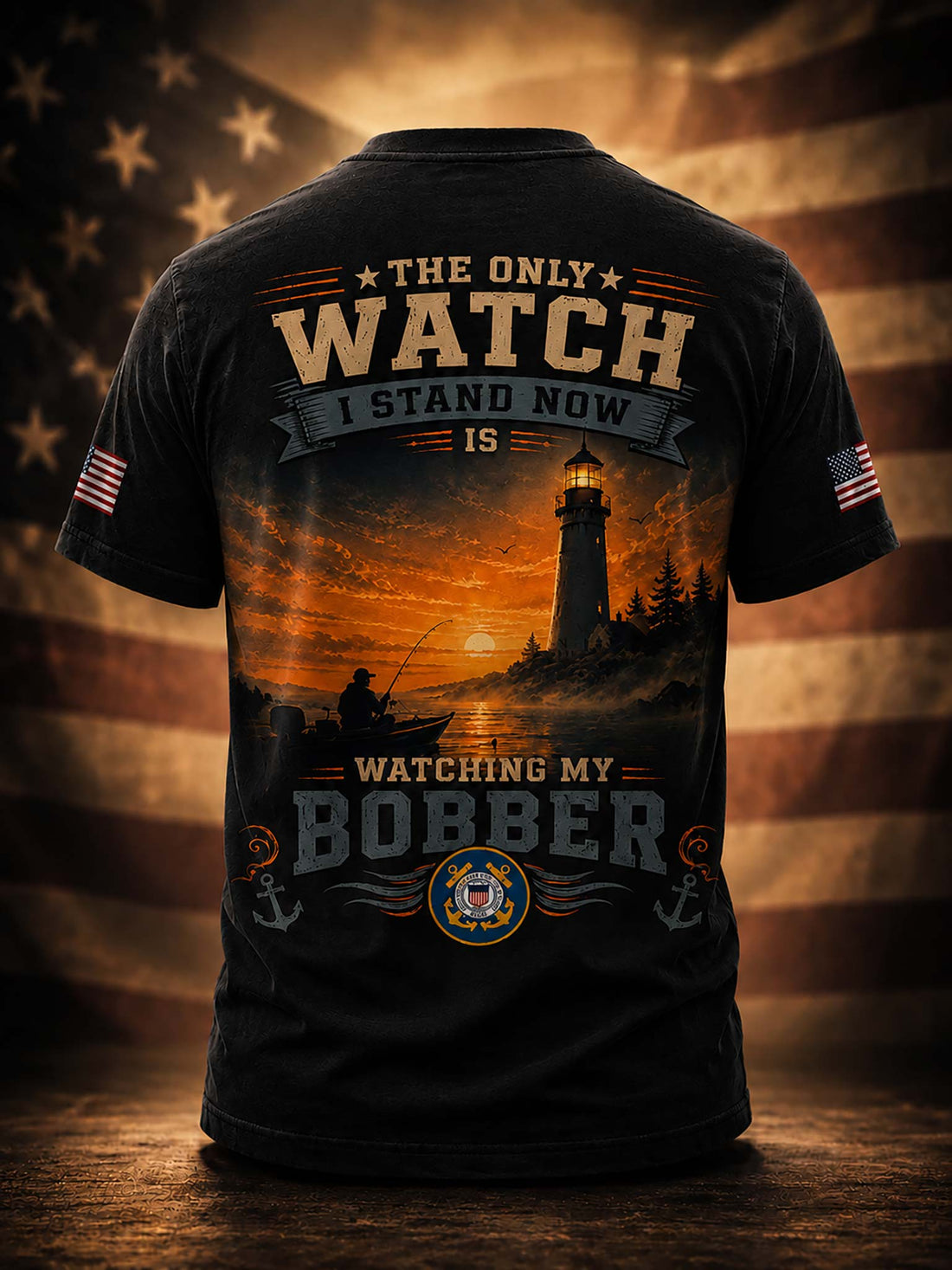 A black short-sleeve t-shirt shown from the back, featuring a large patriotic fishing graphic with a lighthouse, sunset, and text reading 'THE ONLY WATCH I STAND NOW IS WATCHING MY BOBBER'. The shirt is displayed on a wooden surface with a blurred American flag background.