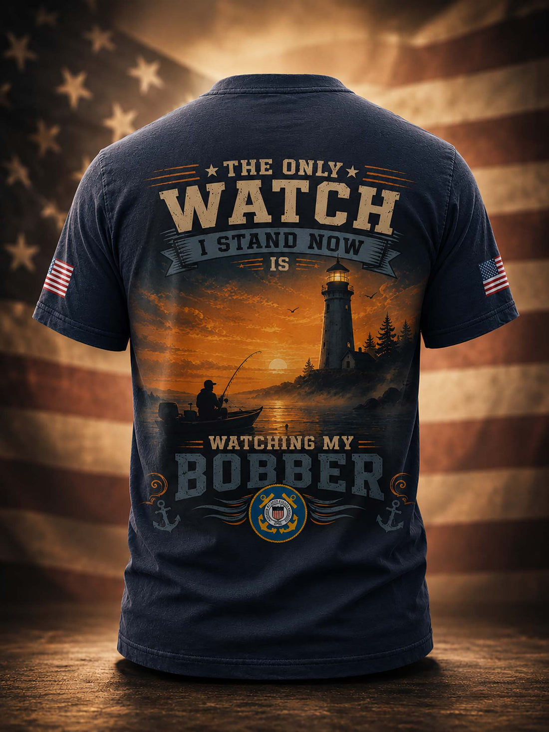 A black short-sleeve t-shirt shown from the back, featuring a large patriotic fishing graphic with a lighthouse, sunset, and text reading 'THE ONLY WATCH I STAND NOW IS WATCHING MY BOBBER'. The shirt is displayed on a wooden surface with a blurred American flag background.