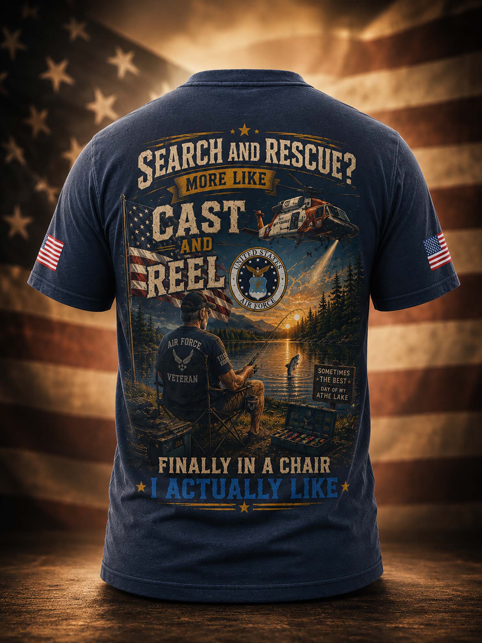 A navy blue short-sleeve t-shirt shown from the back, featuring a large patriotic military-themed graphic with text reading 'SEARCH AND RESCUE? MORE LIKE CAST AND REEL' and 'FINALLY IN A CHAIR I ACTUALLY LIKE'. The shirt includes U.