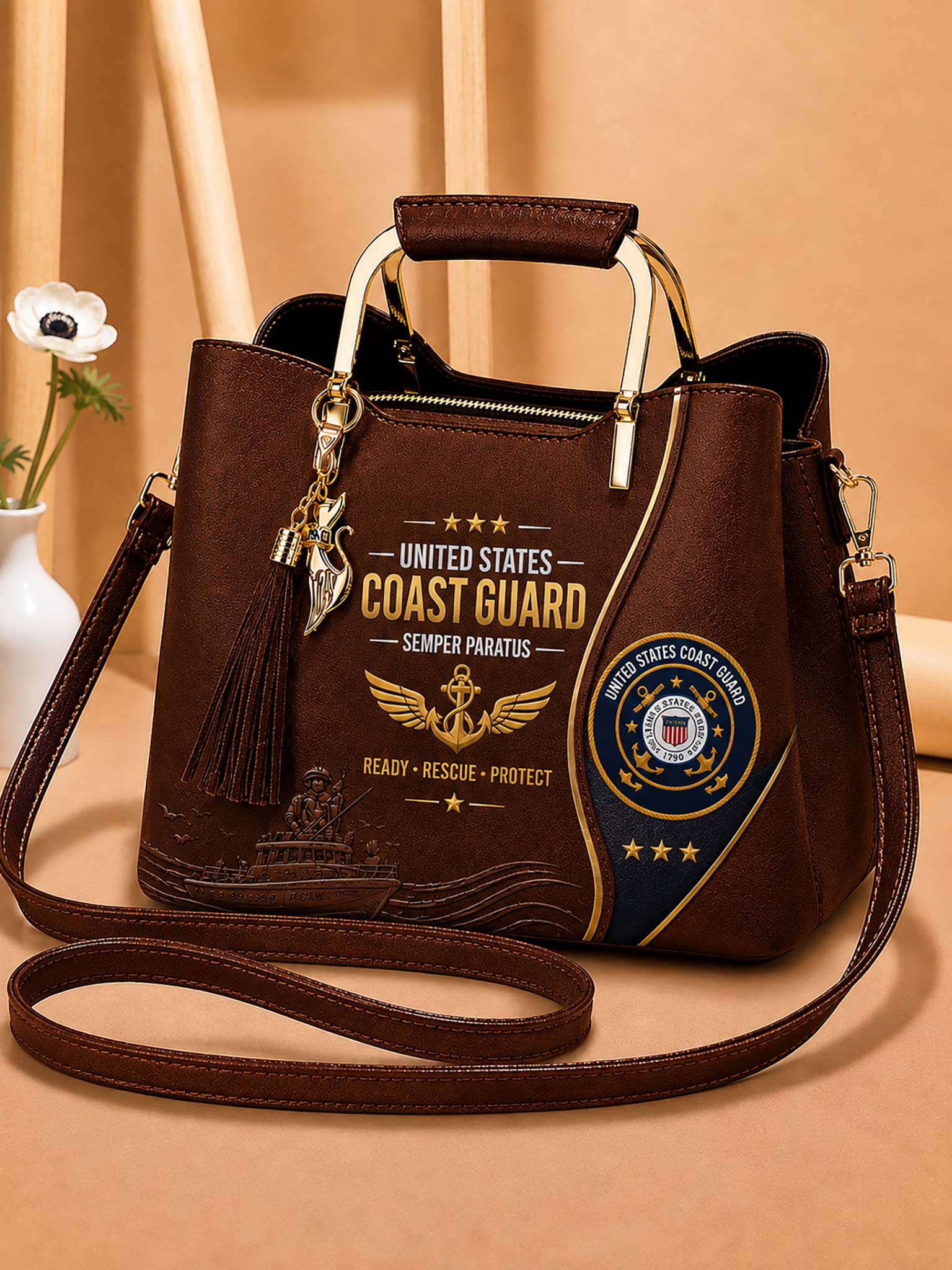 A dark brown faux-leather handbag with a top handle and shoulder strap, featuring United States Coast Guard themed graphics, including a tassel charm, on a warm beige background.