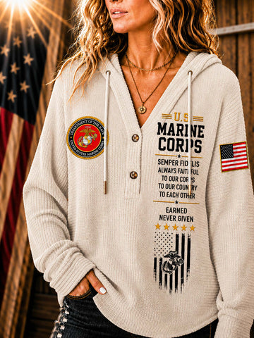 A woman wearing a beige waffle-knit hoodie with military-themed graphics, including a U.S.