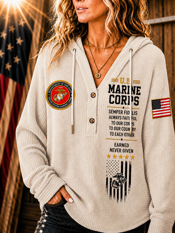 A woman wearing a beige waffle-knit hoodie with military-themed graphics, including a U.S.