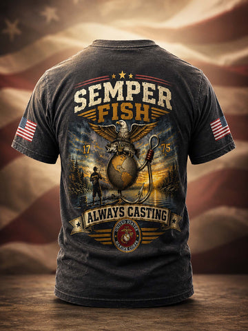 A dark charcoal gray graphic t-shirt shown from the back, featuring a large 'Semper Fish' design with an eagle, anchor, and globe motif, plus 'Always Casting' and a USMC emblem. The shirt is displayed on a wooden surface with a blurred American flag background.