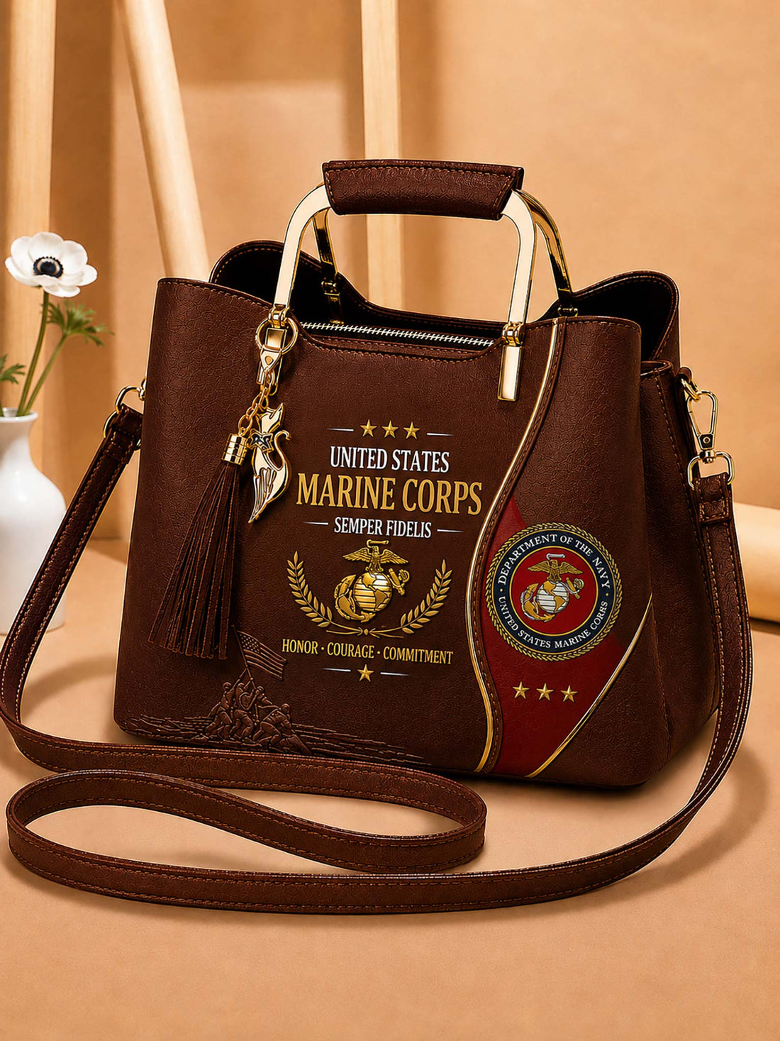 A dark brown faux-leather handbag with a top handle and shoulder strap, decorated with United States Marine Corps emblems, text, and a tassel charm, set against a warm beige background.