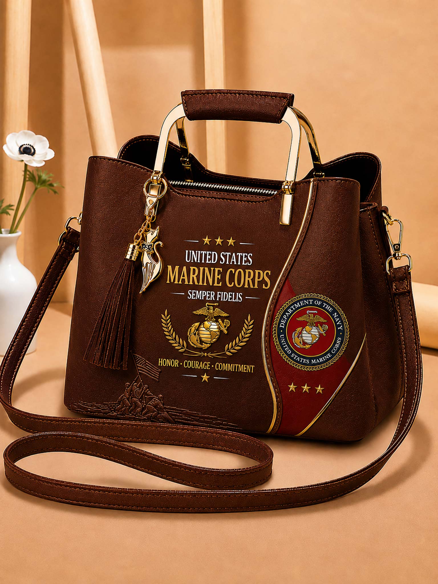 A dark brown faux-leather handbag with a top handle and shoulder strap, decorated with United States Marine Corps emblems, text, and a tassel charm, set against a warm beige background.