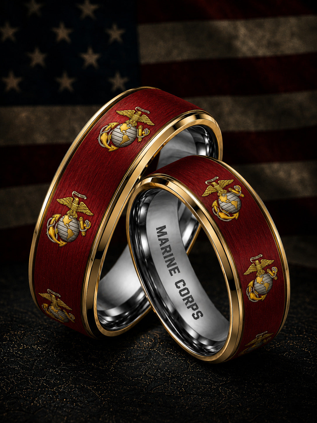 Two wedding bands with a dark red wood inlay featuring the gold and silver Eagle, Globe, and Anchor emblem, with one band engraved with 'MARINE CORPS' inside, set against a blurred American flag background.