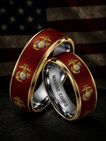 Two wedding bands with a dark red wood inlay featuring the gold and silver Eagle, Globe, and Anchor emblem, with one band engraved with 'MARINE CORPS' inside, set against a blurred American flag background.