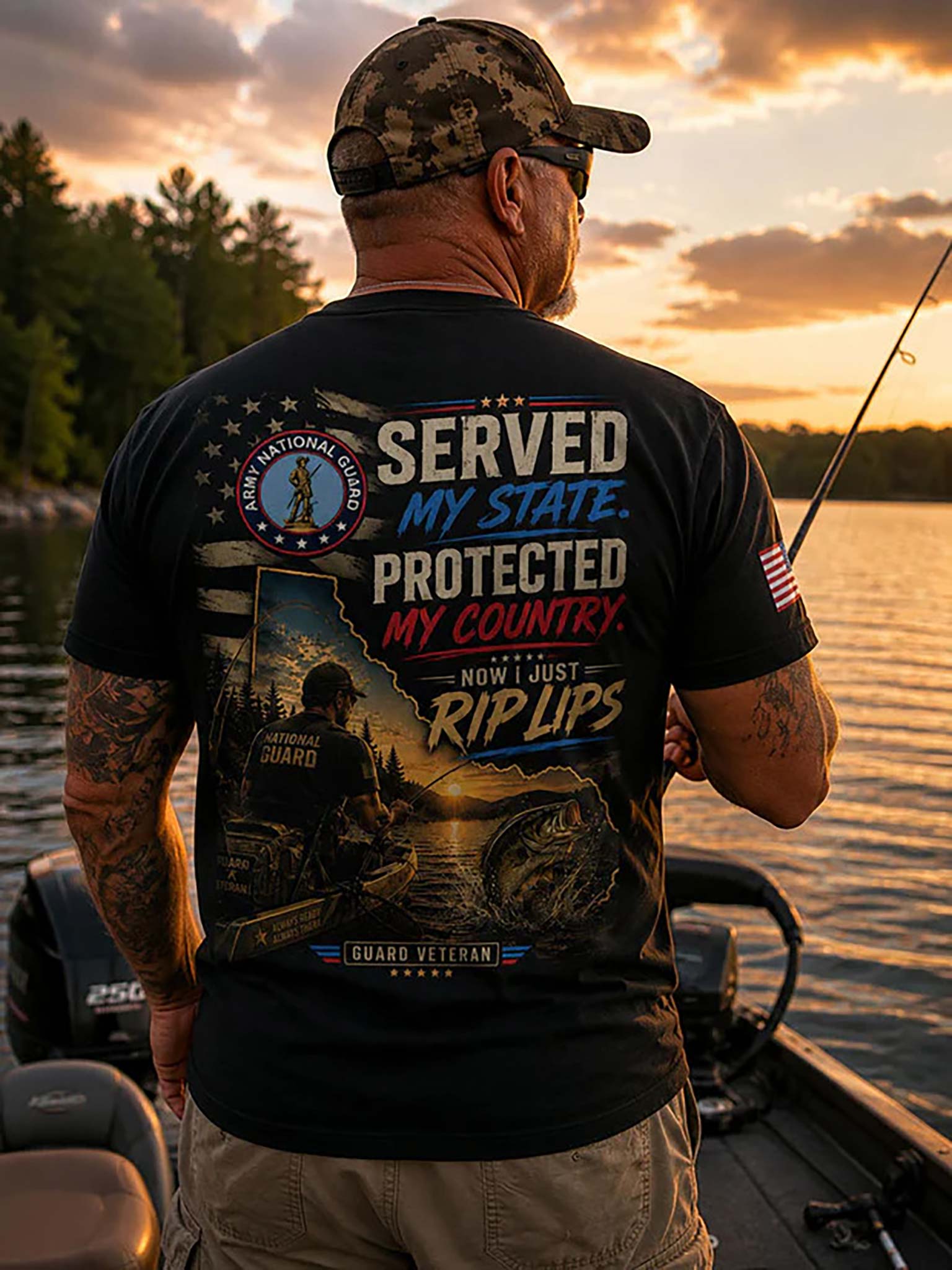 A man wearing a black graphic t-shirt and camouflage cap stands on a boat at sunset, facing away from the camera to show the back of the shirt. The shirt features a large patriotic US Army National Guard graphic with the text 'SERVED MY STATE.