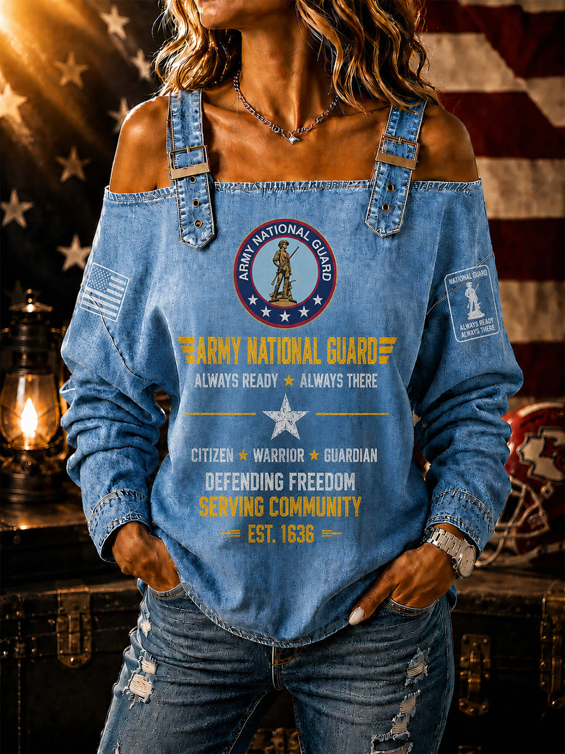 A woman wearing a light blue off-the-shoulder denim top with Army National Guard graphics, paired with distressed blue jeans, posed in front of a rustic American flag and lantern background.