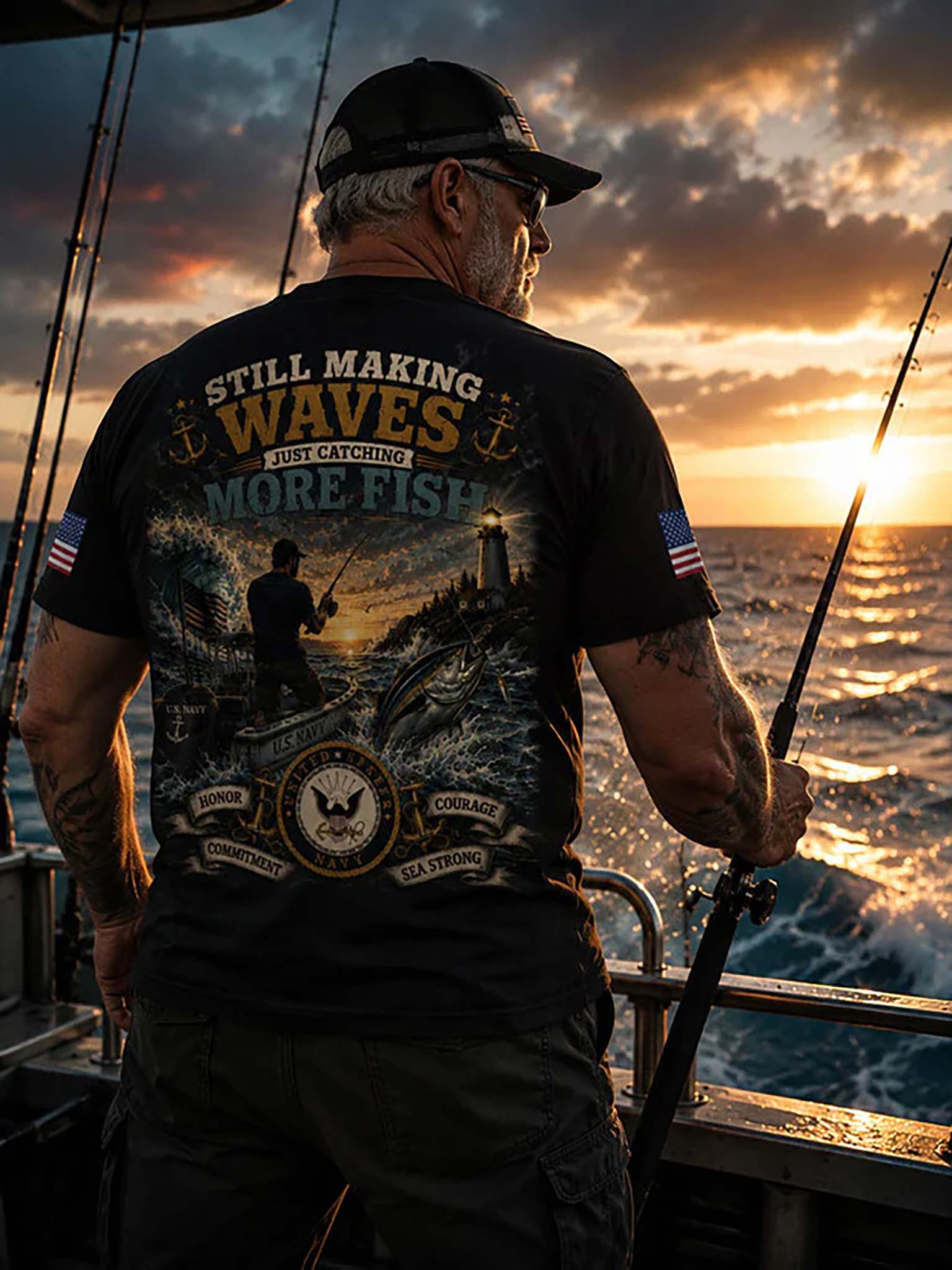 A man stands on a lakeshore at sunset wearing a black graphic T-shirt with patriotic and fishing-themed designs