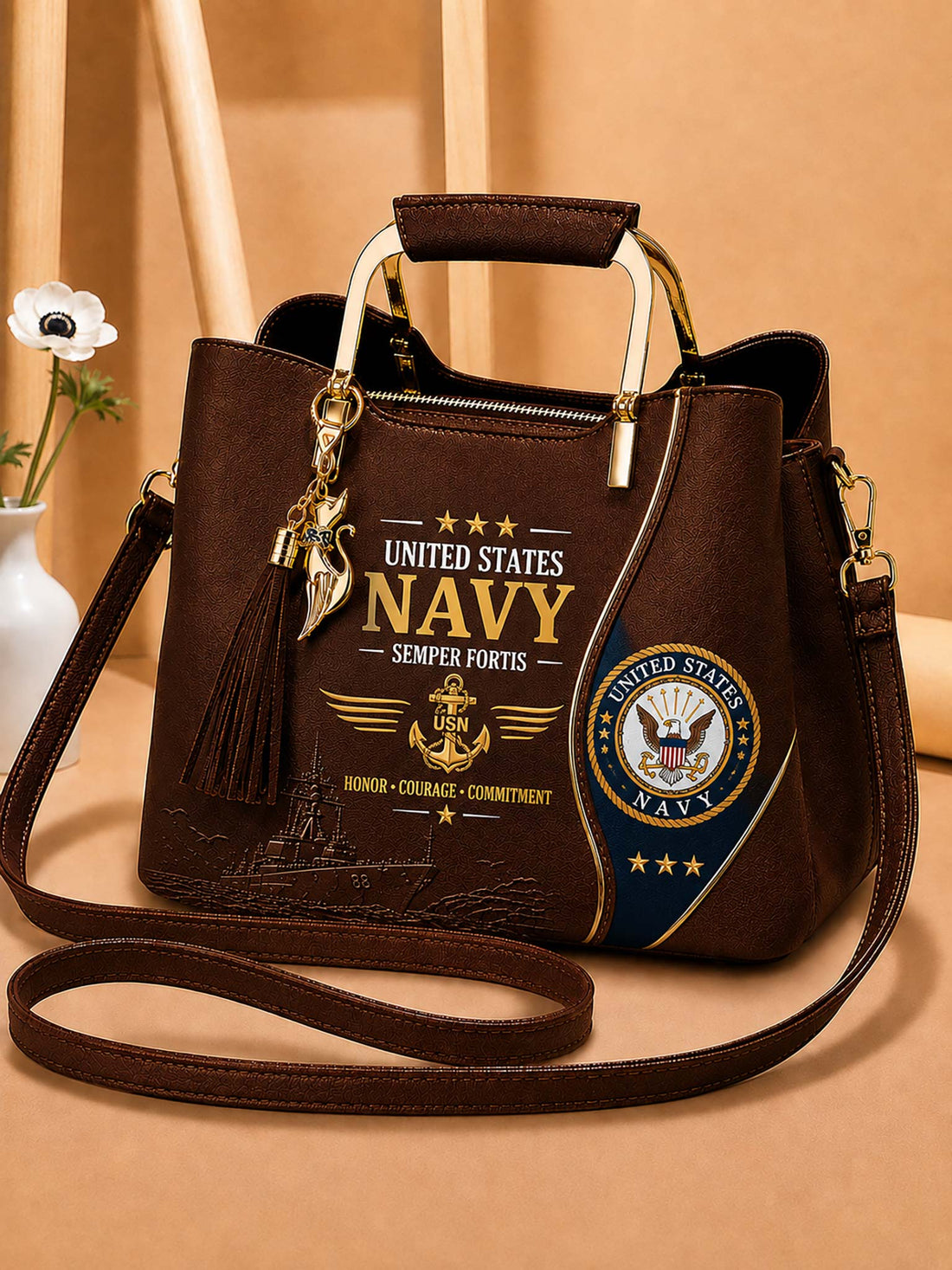 A dark brown faux-leather handbag with a United States Navy theme, featuring gold-tone hardware, a tassel charm, and printed graphics including the US Navy emblem and 'Semper Fortis' text, set against a warm beige background.