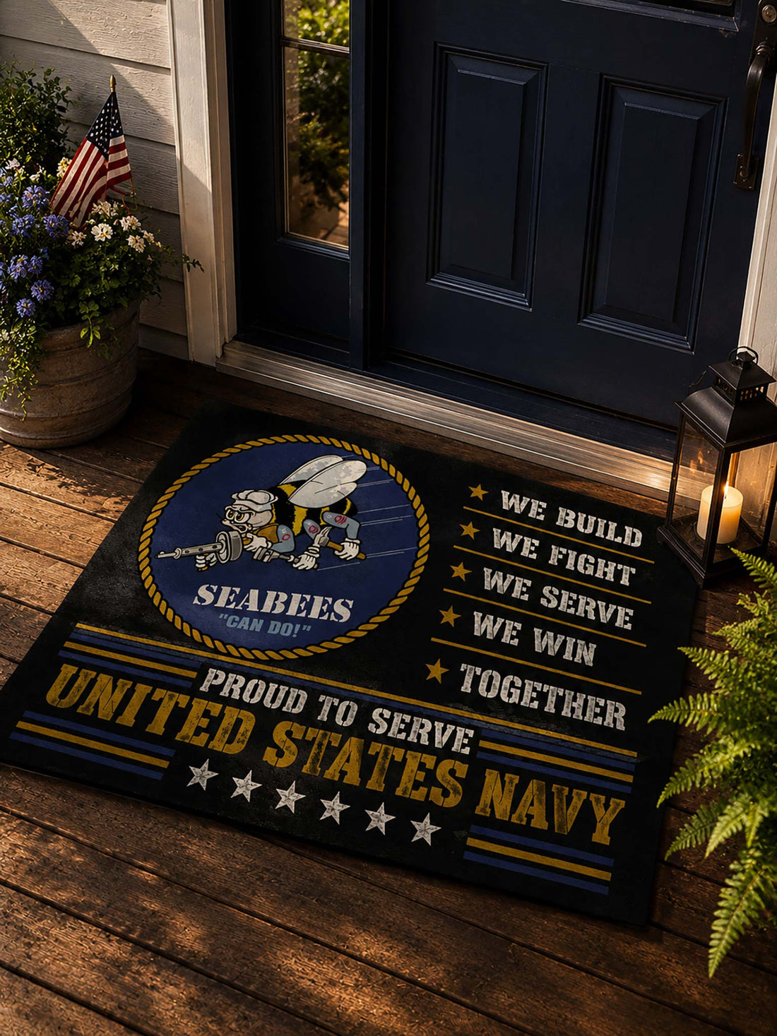 A rectangular navy and gold doormat with a Seabees emblem and the words 'We Build We Fight We Serve We Win Together' and 'Proud to Serve United States Navy,' placed on a tan stone floor in front of glass doors.