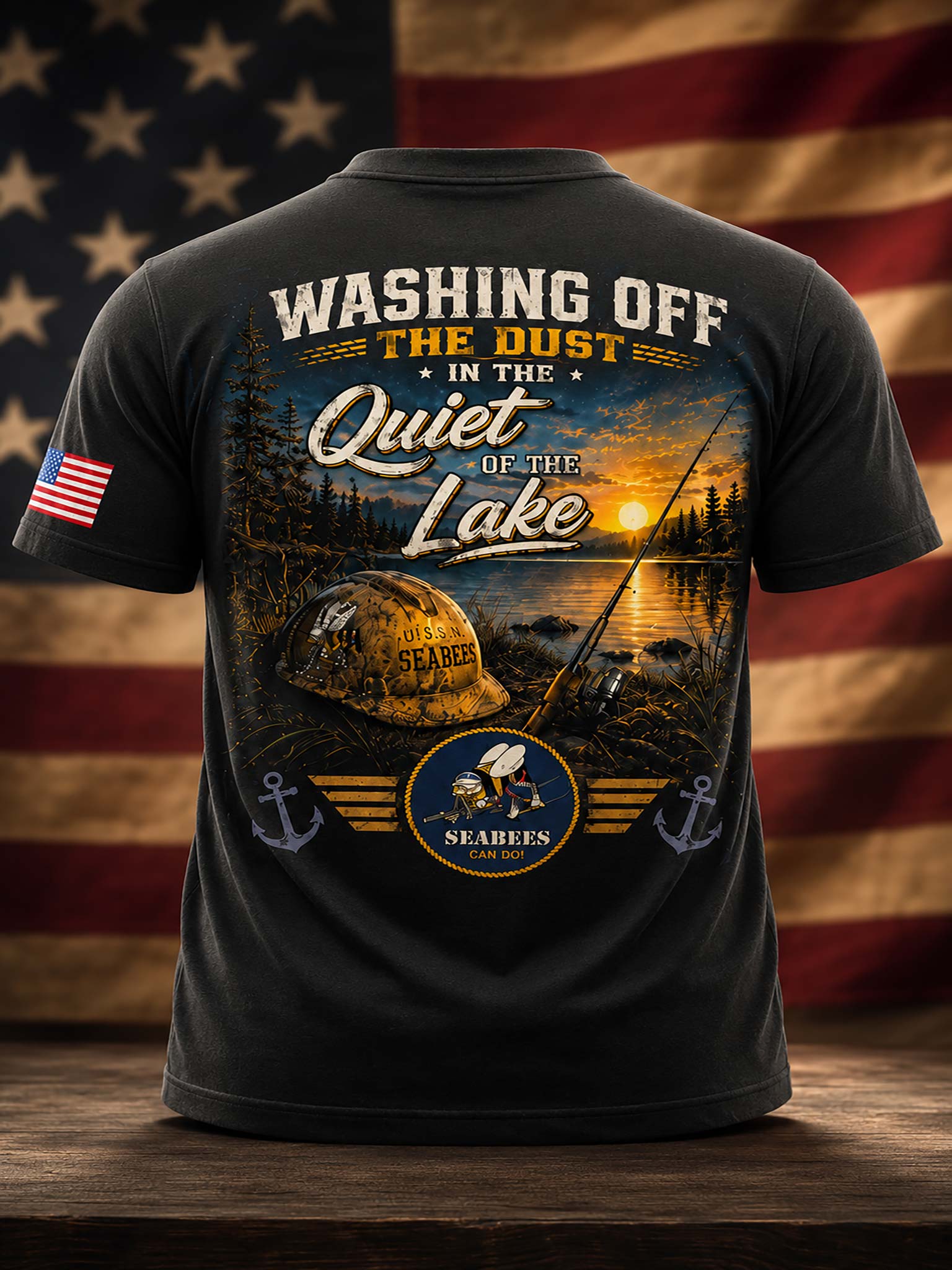 A black short-sleeve t-shirt shown from the back, featuring a large outdoor fishing graphic with the text 'WASHING OFF THE DUST IN THE Quiet OF THE Lake' and a sunset lake scene. The shirt is displayed on a wooden surface with a blurred American flag background.