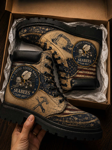 A pair of distressed military-style combat boots with a vintage US Navy Seabees print, displayed inside a brown cardboard box with tissue paper. A hand is holding the boot on the left side.
