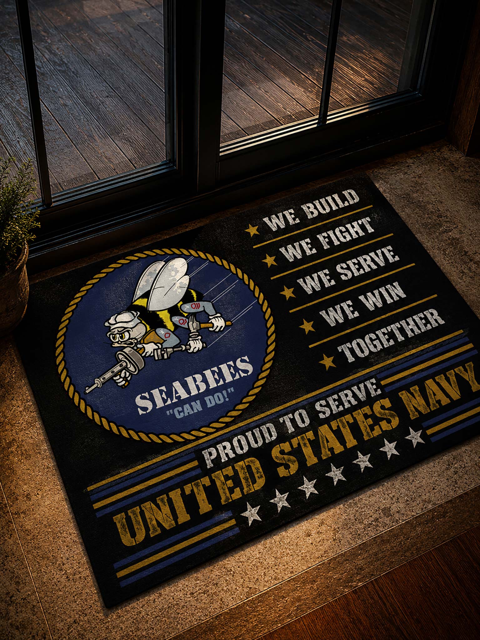 A rectangular navy and gold doormat with a Seabees emblem and the words 'We Build We Fight We Serve We Win Together' and 'Proud to Serve United States Navy,' placed on a tan stone floor in front of glass doors.