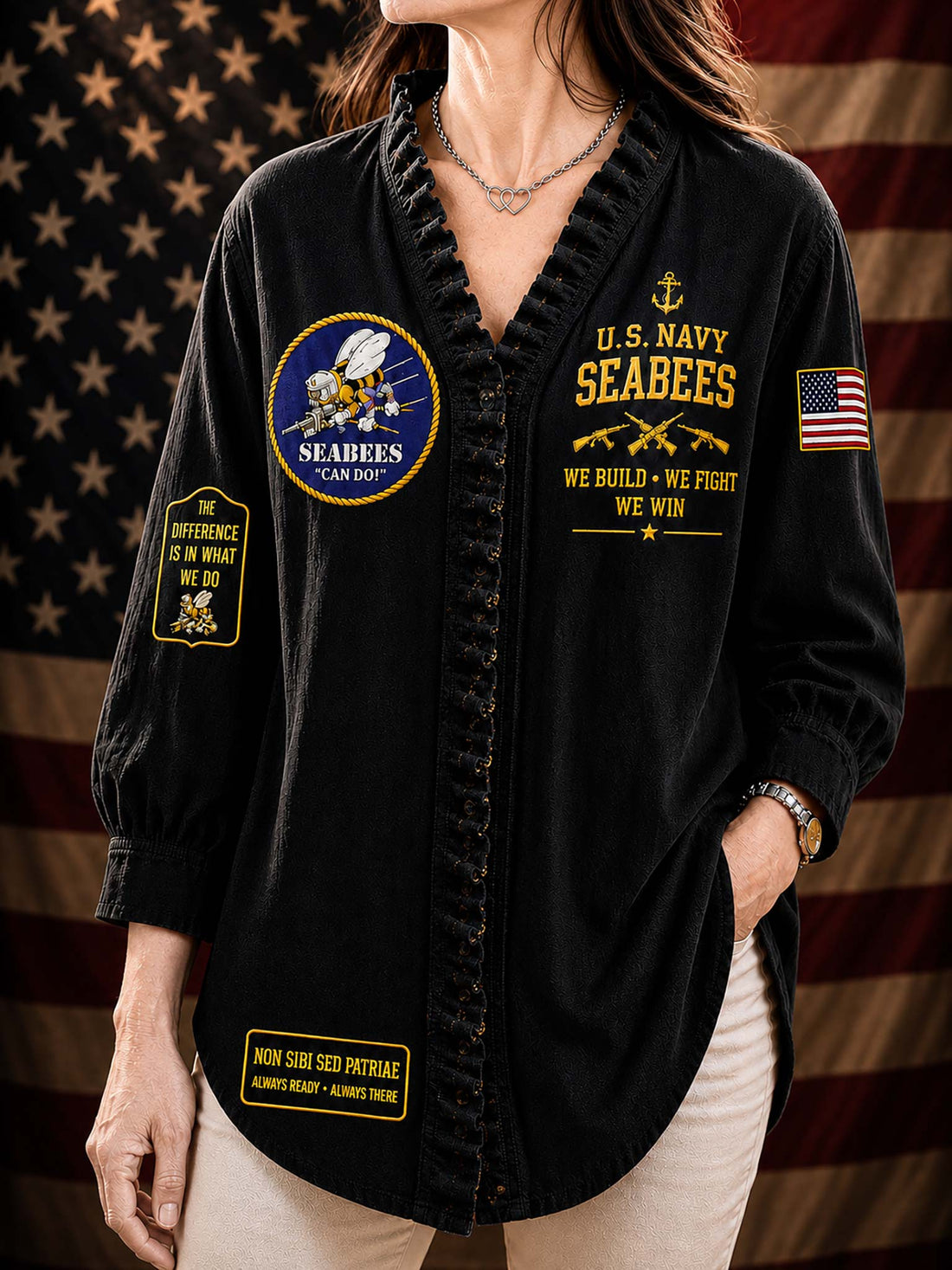 A woman wearing a black long-sleeve button-front shirt with ruffled trim, featuring gold and multicolor U.S.