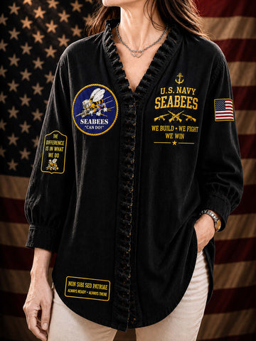 A woman wearing a black long-sleeve button-front shirt with ruffled trim, featuring gold and multicolor U.S.