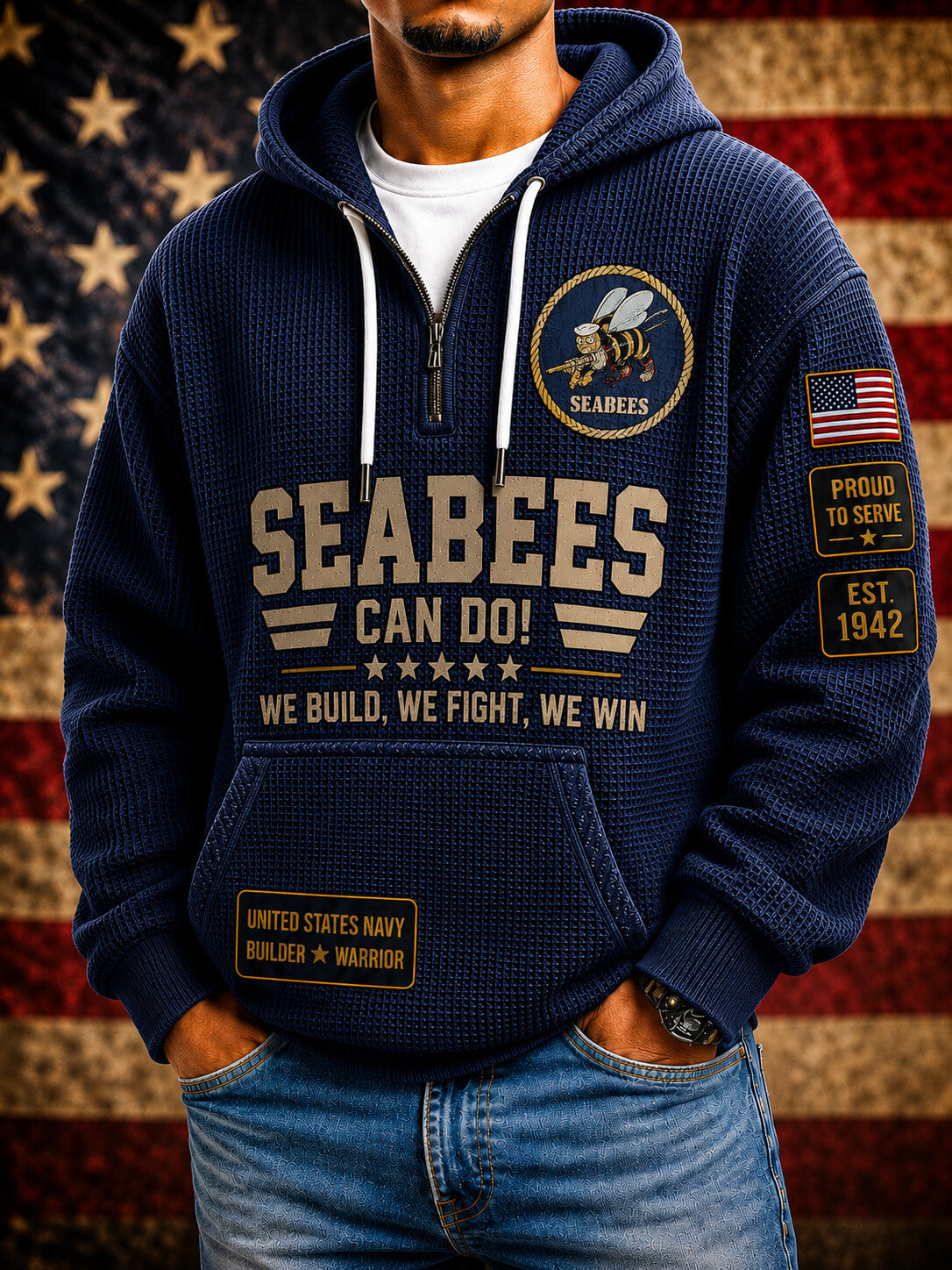 A man wearing a navy blue waffle-knit zip-up hoodie with 'SEABEES CAN DO!' printed on the front, featuring military-themed patches on the sleeves and chest, paired with blue jeans against an American flag background.
