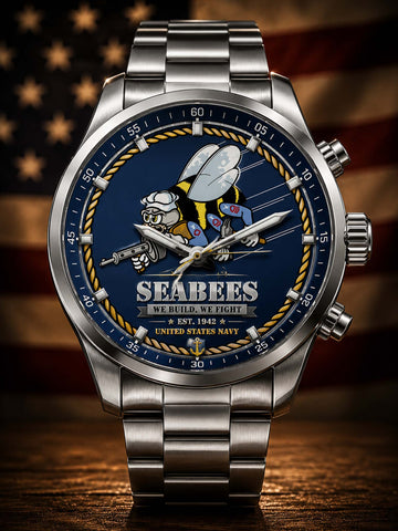 A stainless steel wristwatch with a blue Seabees dial featuring a bee graphic and the text 'Seabees We Build We Fight United States Navy,' shown against a blurred American flag background on a wooden surface.