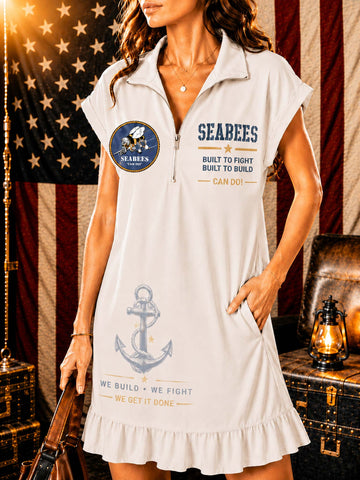 A woman models a white short-sleeve polo dress with a ruffled hem, featuring 'SEABEES' text, an anchor graphic, and a circular patch on the front. The background features an American flag, a leather trunk, and a lantern.