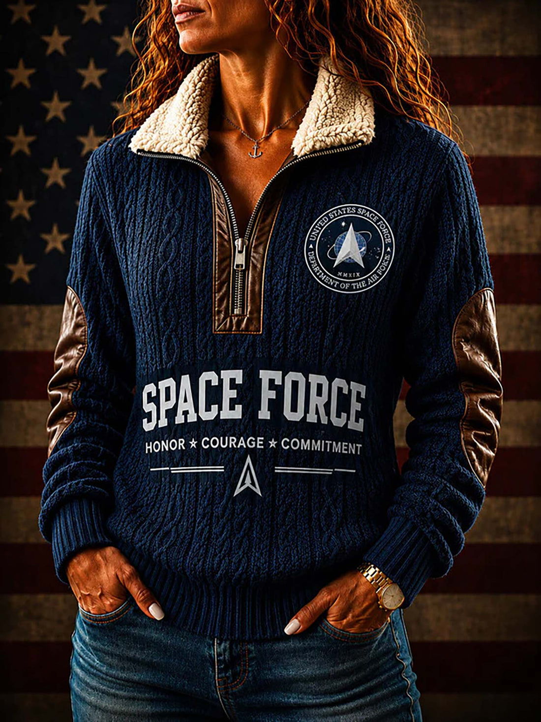 A navy blue cable-knit quarter-zip pullover sweater with a beige sherpa collar, brown elbow patches, and white 'SPACE FORCE' text on the front and back, shown against a blurred American flag background. A circular emblem is visible in the top right.