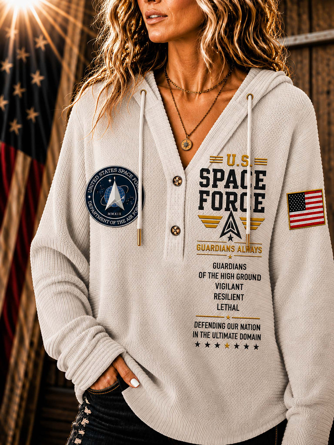 A woman wearing a light beige hooded sweatshirt with military-themed graphics, including 'U.S.
