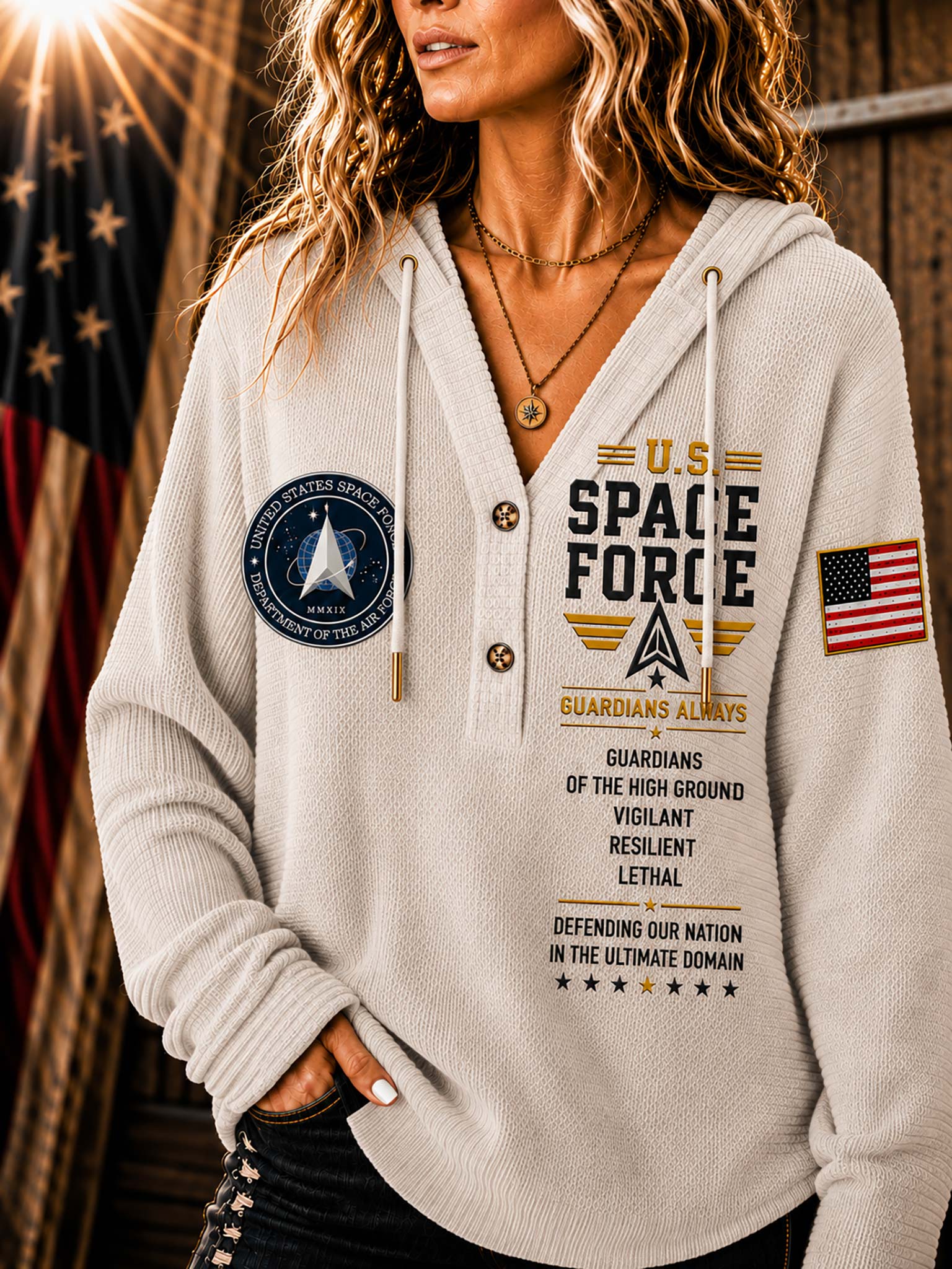 A woman wearing a light beige hooded sweatshirt with military-themed graphics, including 'U.S.