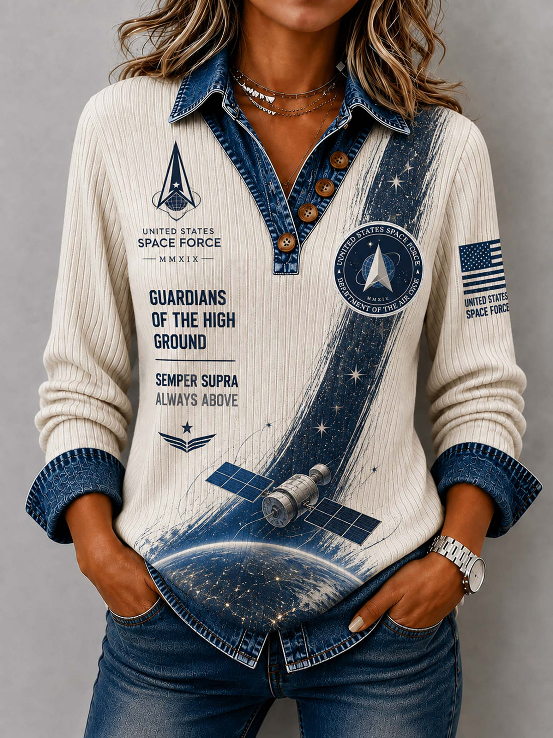 A woman wearing a long-sleeve ribbed knit top with a space-themed print. The top features a cream base with a blue denim-style collar, cuffs, and front placket, decorated with graphics of a space station, Earth, stars, and United States Space Force insignia.