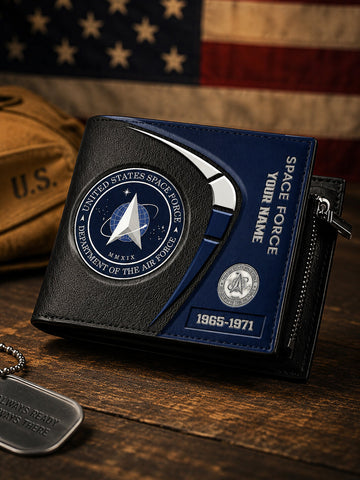 A black and navy blue bifold wallet themed after the United States Space Force, displayed on a rustic wooden table with an American flag and military gear in the background.