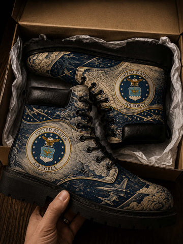 A pair of lace-up boots with a detailed United States Air Force theme, featuring the Air Force seal and fighter jets on a map background. The boots are shown inside a cardboard box with tissue paper, with a hand holding the front boot.