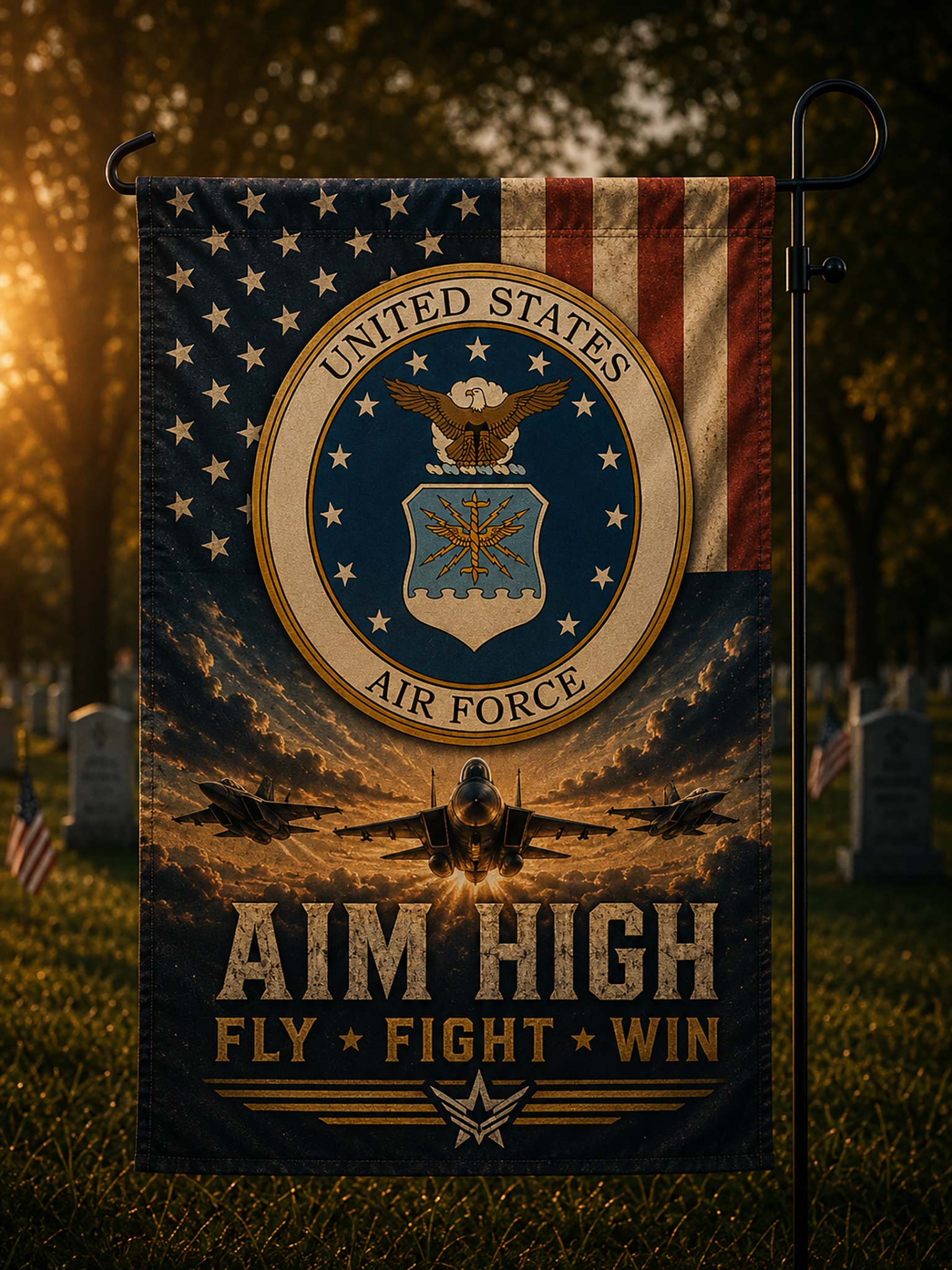A vertical garden flag on a black metal stand, featuring a United States Air Force emblem, American flag elements, fighter jets, and the text 'AIM HIGH FLY FIGHT WIN' against a sunset sky, shown outdoors in a grassy cemetery setting.