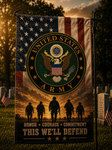 A vertical garden flag featuring the United States Army emblem over an American flag and sunset scene, with soldier silhouettes and the text 'HONOR * COURAGE * COMMITMENT THIS WE'LL DEFEND', displayed on a black metal flagpole outdoors in a cemetery setting.