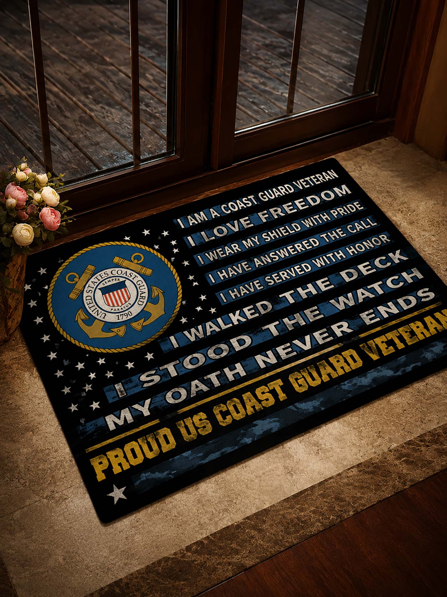 A rectangular doormat with a Coast Guard-themed design, placed on a stone entryway floor in front of glass doors. The mat features a large blue and gold Coast Guard emblem, white and yellow text reading patriotic service quotes, and a dark navy background with white stars.