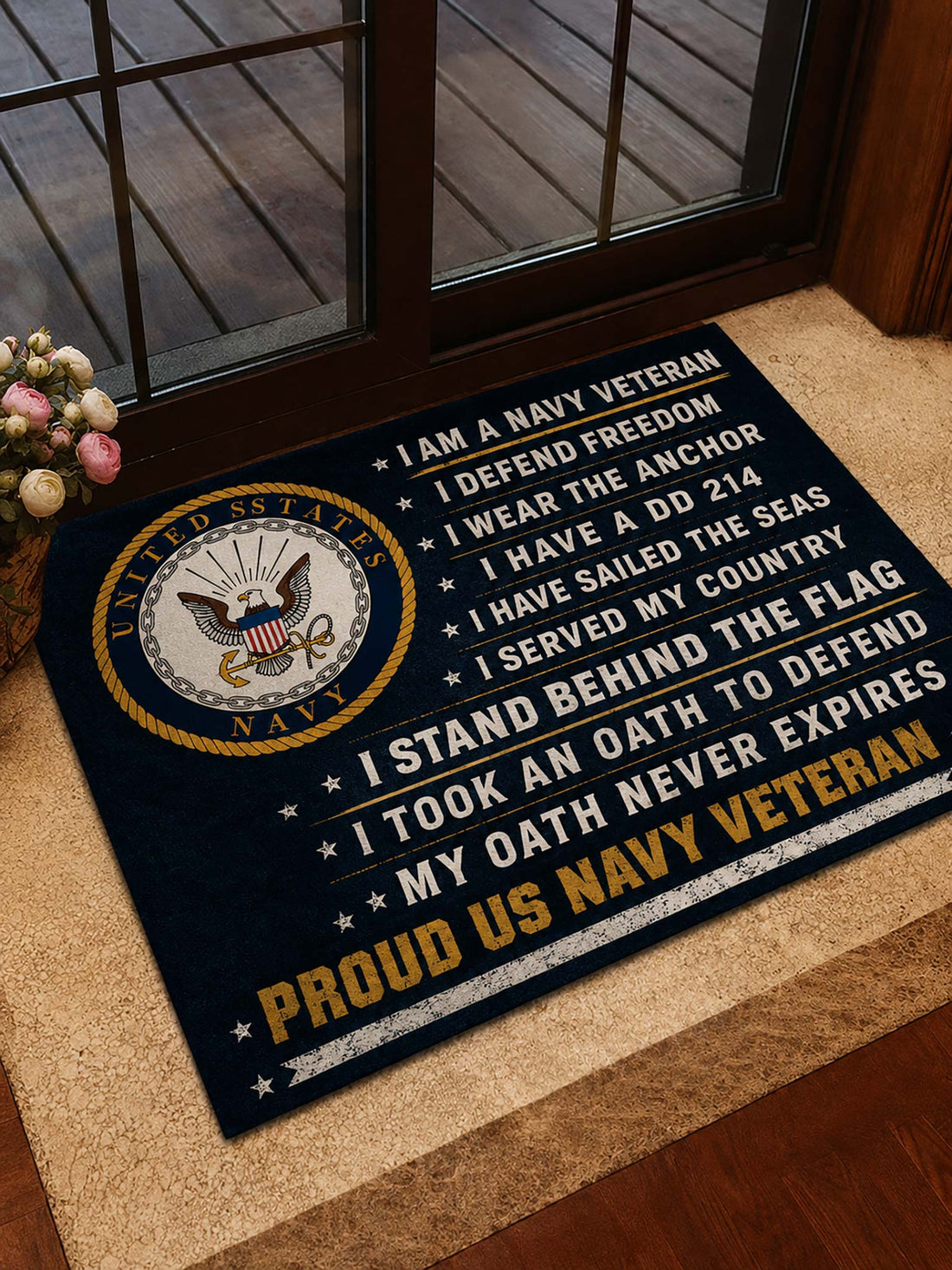 A navy blue doormat with a United States Navy emblem and patriotic text, placed on a tan entryway step in front of a glass door.