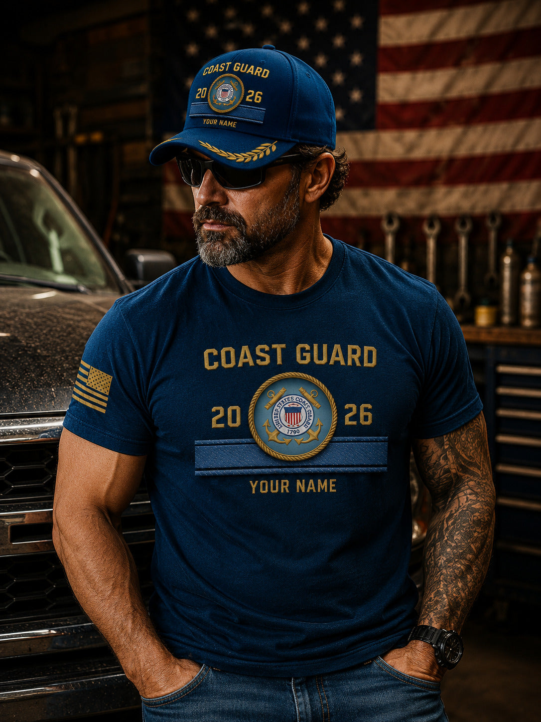 A blue Coast Guard themed baseball cap with gold embroidered details, including 'COAST GUARD', a central emblem, and 'YOUR NAME', displayed on a wooden surface with a blurred American flag in the background.