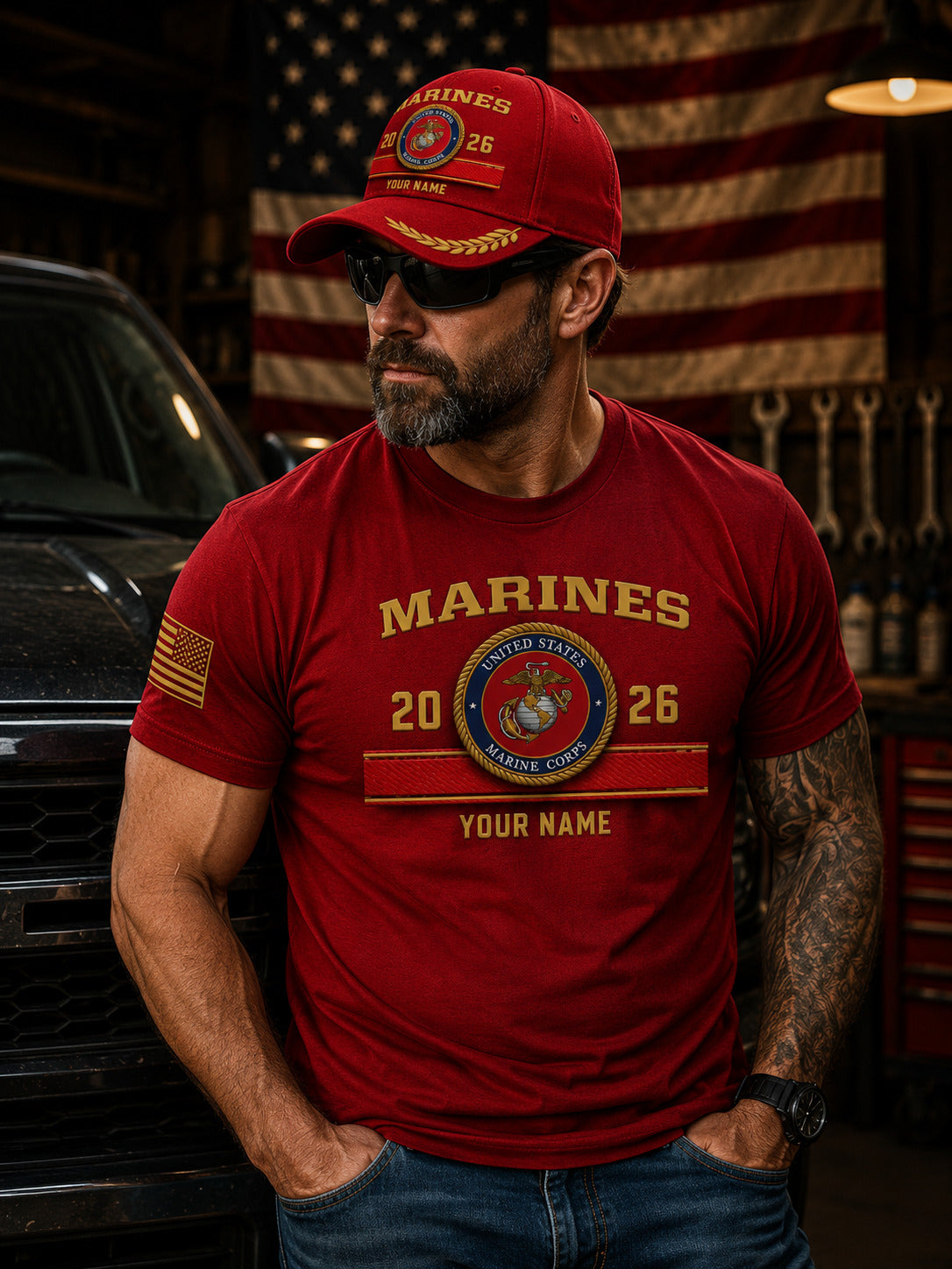 A red baseball cap with gold embroidered details, featuring a United States Marine Corps emblem, 'MARINES' text, and 'YOUR NAME' customization option, set against a blurred American flag and wooden background.