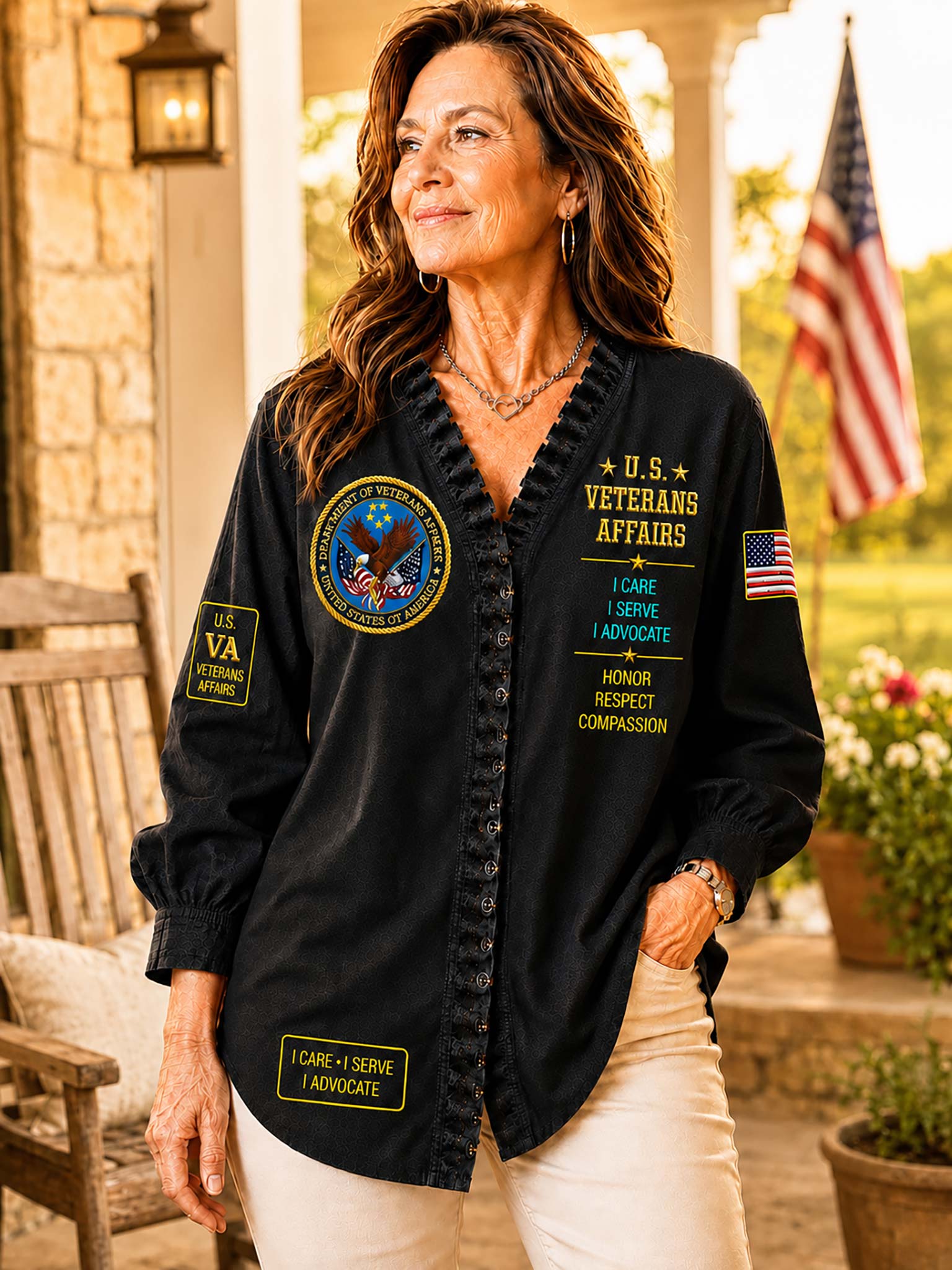 A woman stands on a porch wearing a black button-front shirt with military-style patches and yellow text reading 'Veterans Affairs' and 'I Care I Serve I Advocate.' The background shows a stone porch, an American flag, and potted plants.
