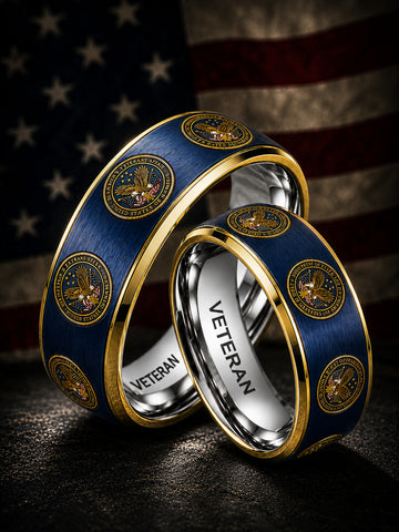 Two matching military-style rings with blue enamel, gold trim, and circular gold insignia, shown overlapping on a dark surface with an American flag blurred in the background. The inner band is engraved with the word "VETERAN.
